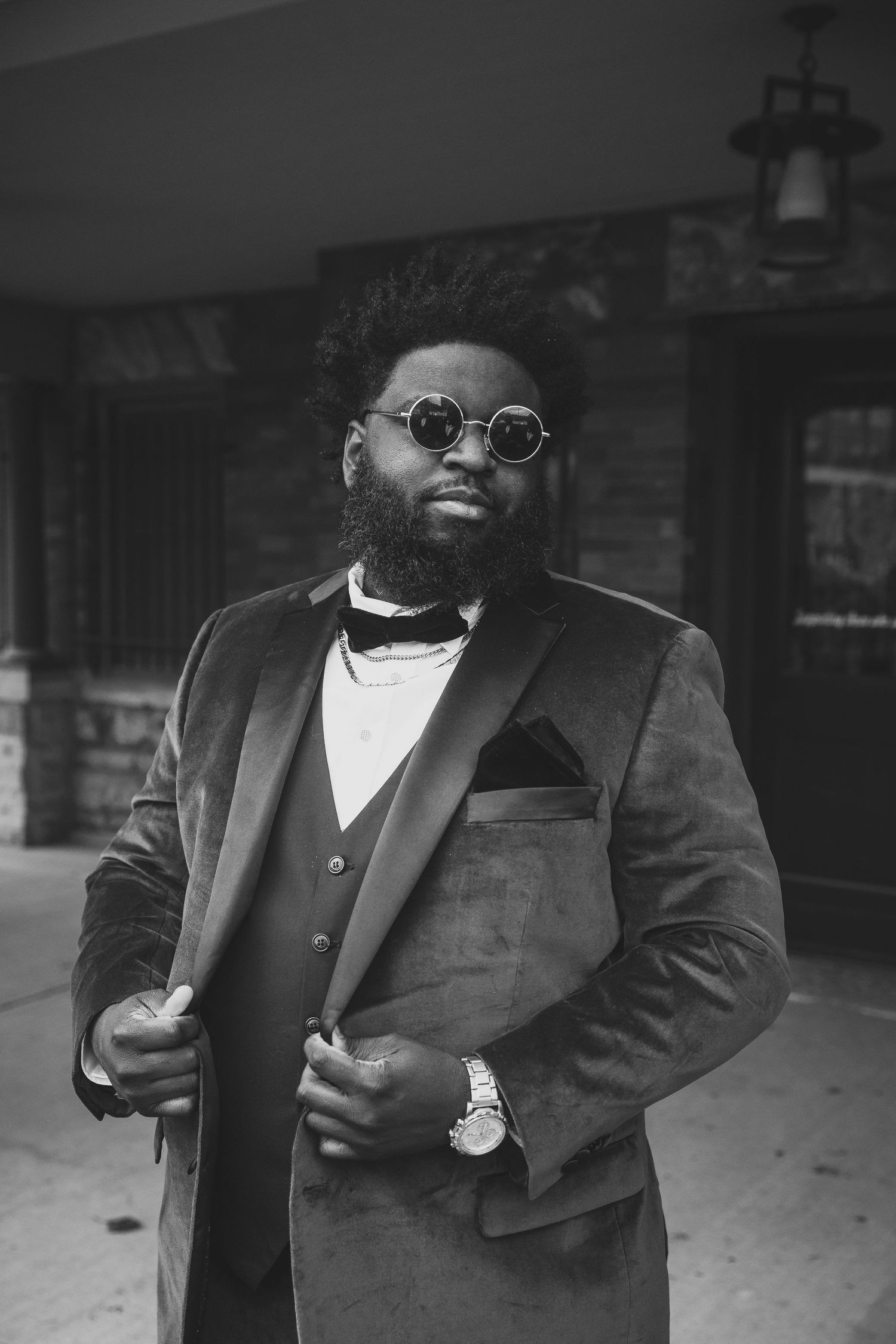 Person in formal attire wearing sunglasses and bow tie poses in black and white portrait.