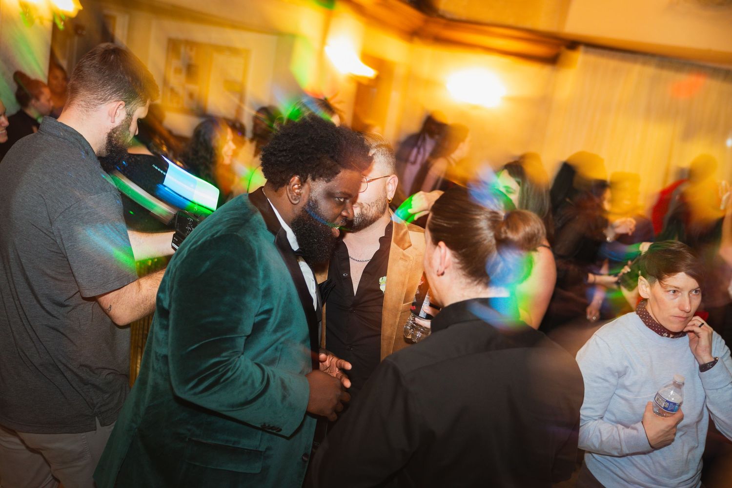 Wedding reception dance floor filled with guests dancing under warm amber lighting.