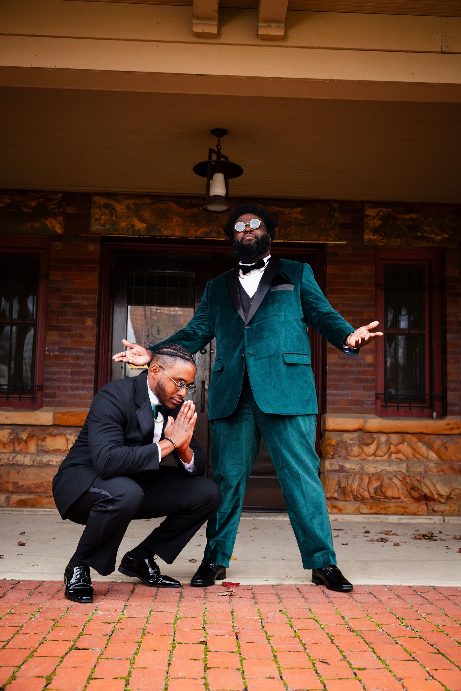 Groomsmen in contrasting suits pose playfully on brick patio.