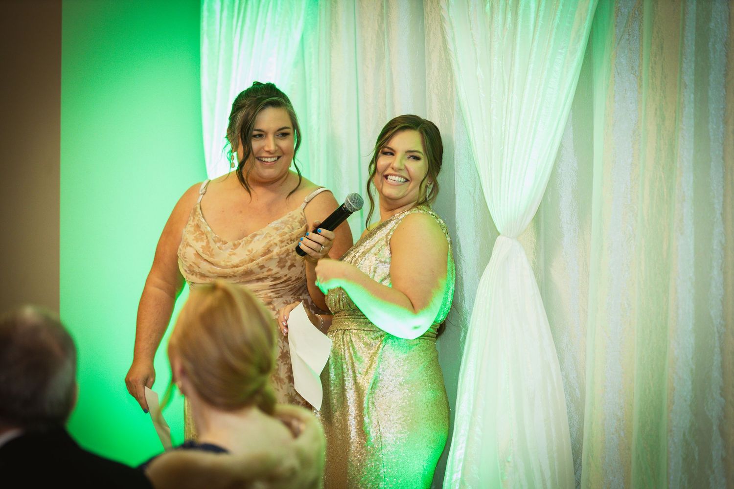 Wedding celebration space features sheer white curtains with emerald green lighting effects.