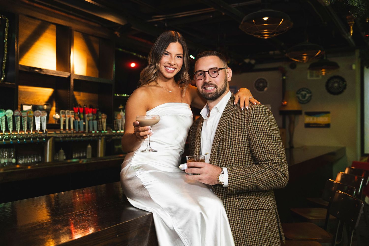 Couple celebrating at bar with drinks in formal attire.