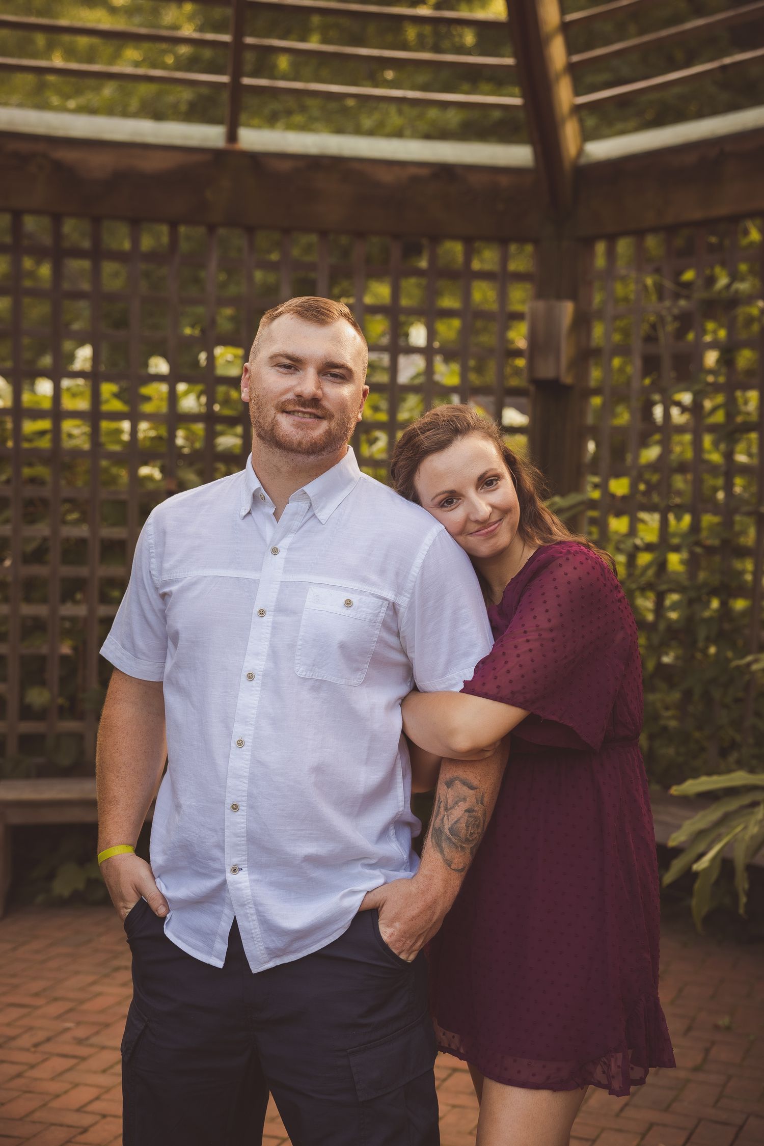 Couple posing together on brick patio with garden trellis backdrop.