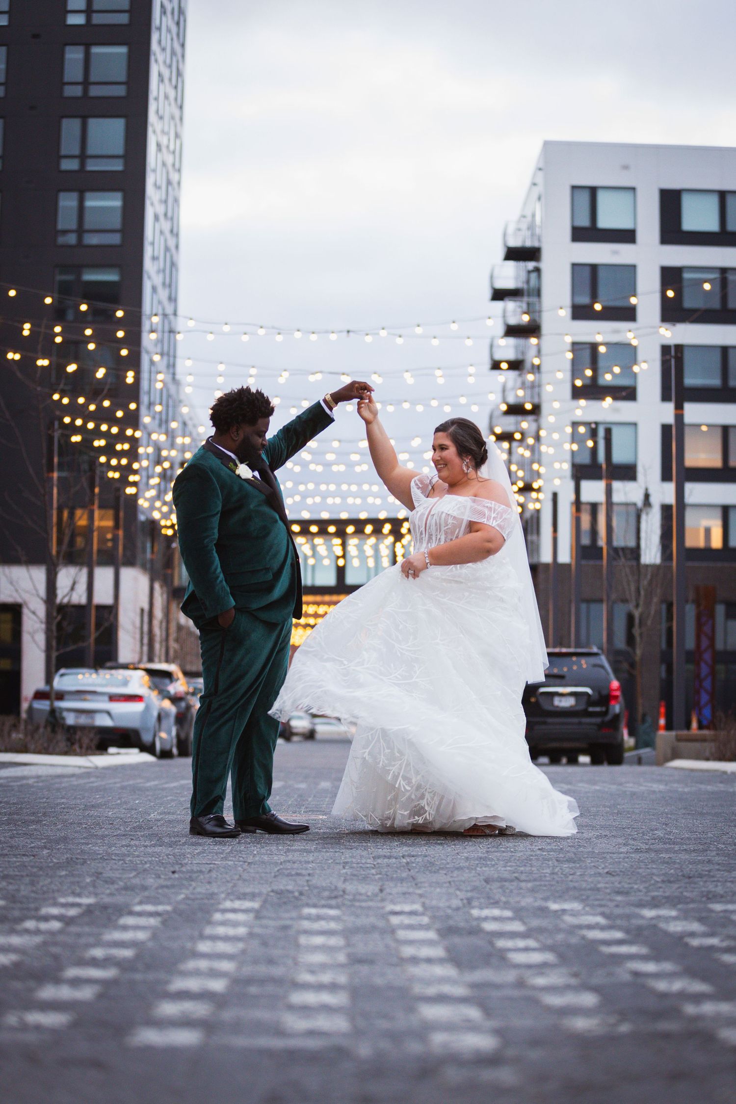 Wedding couple dancing in an urban setting with string lights and modern buildings.