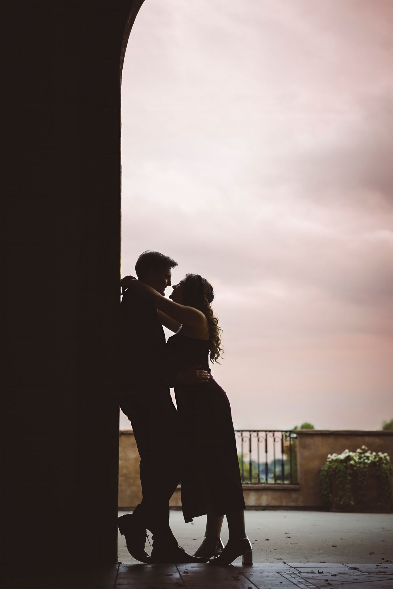 Silhouetted couple in romantic embrace under archway at sunset.