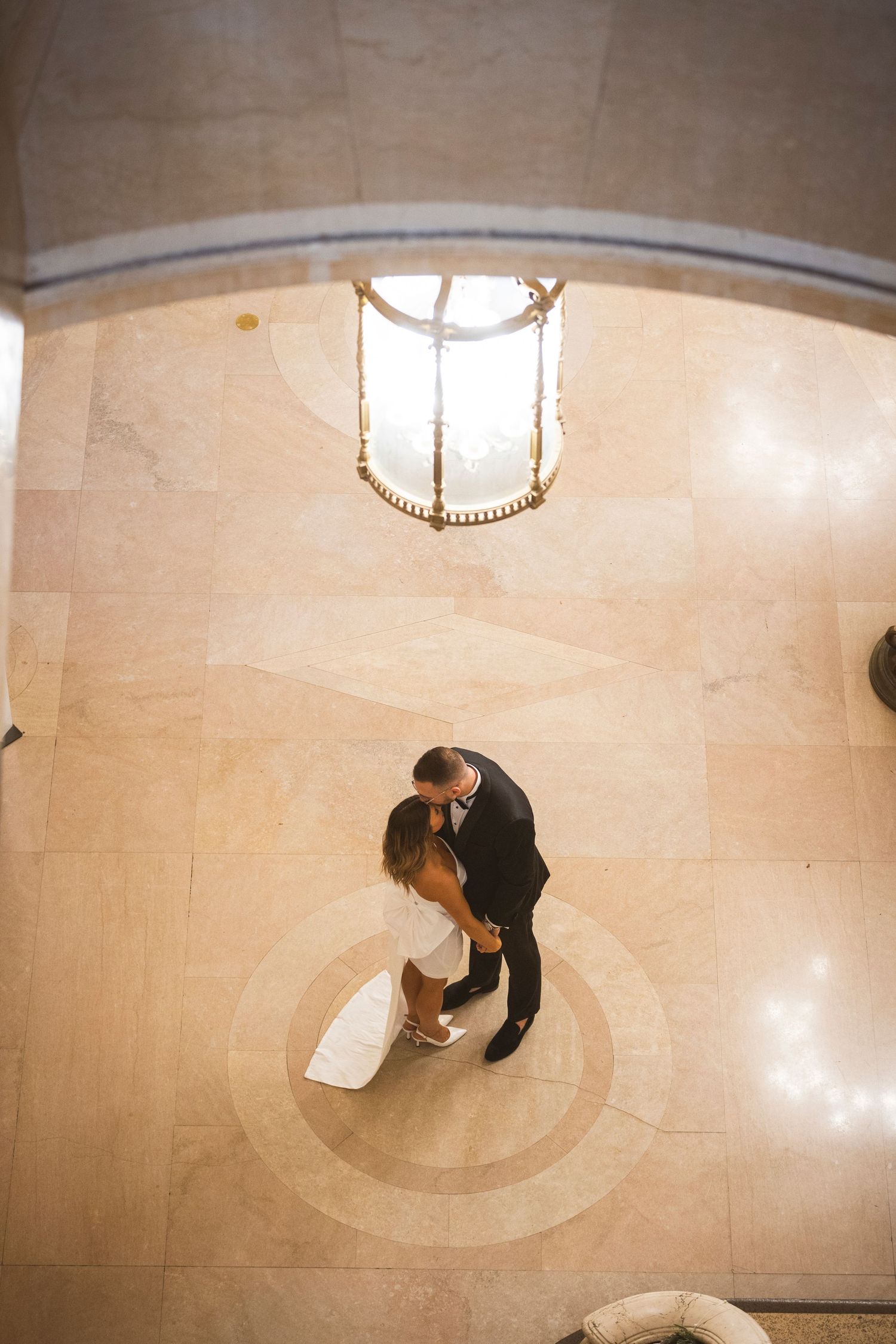 Overhead view of a couple dancing on a polished marble floor under an ornate chandelier.