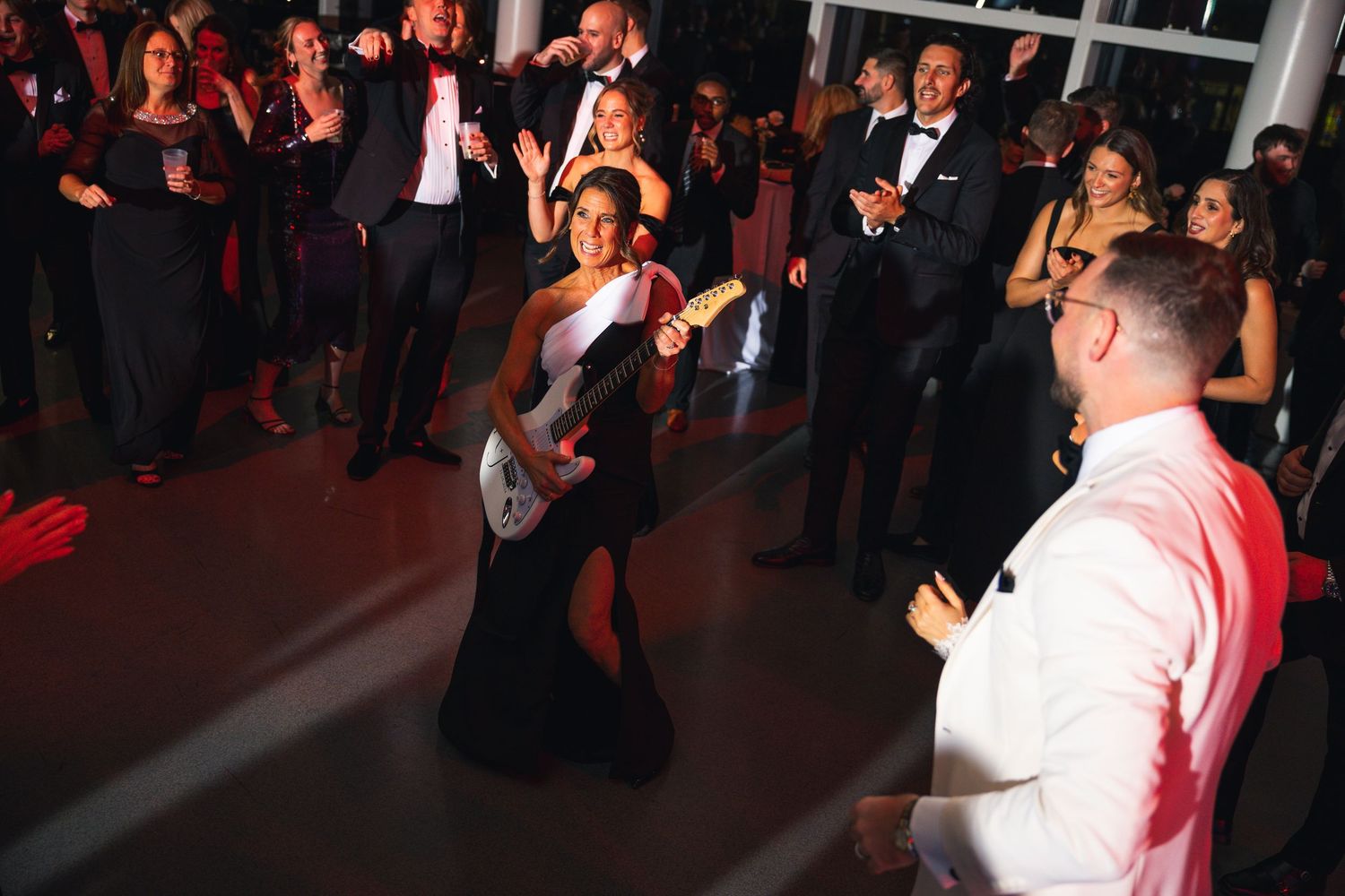Wedding reception guests dance and celebrate on a dimly lit dance floor.