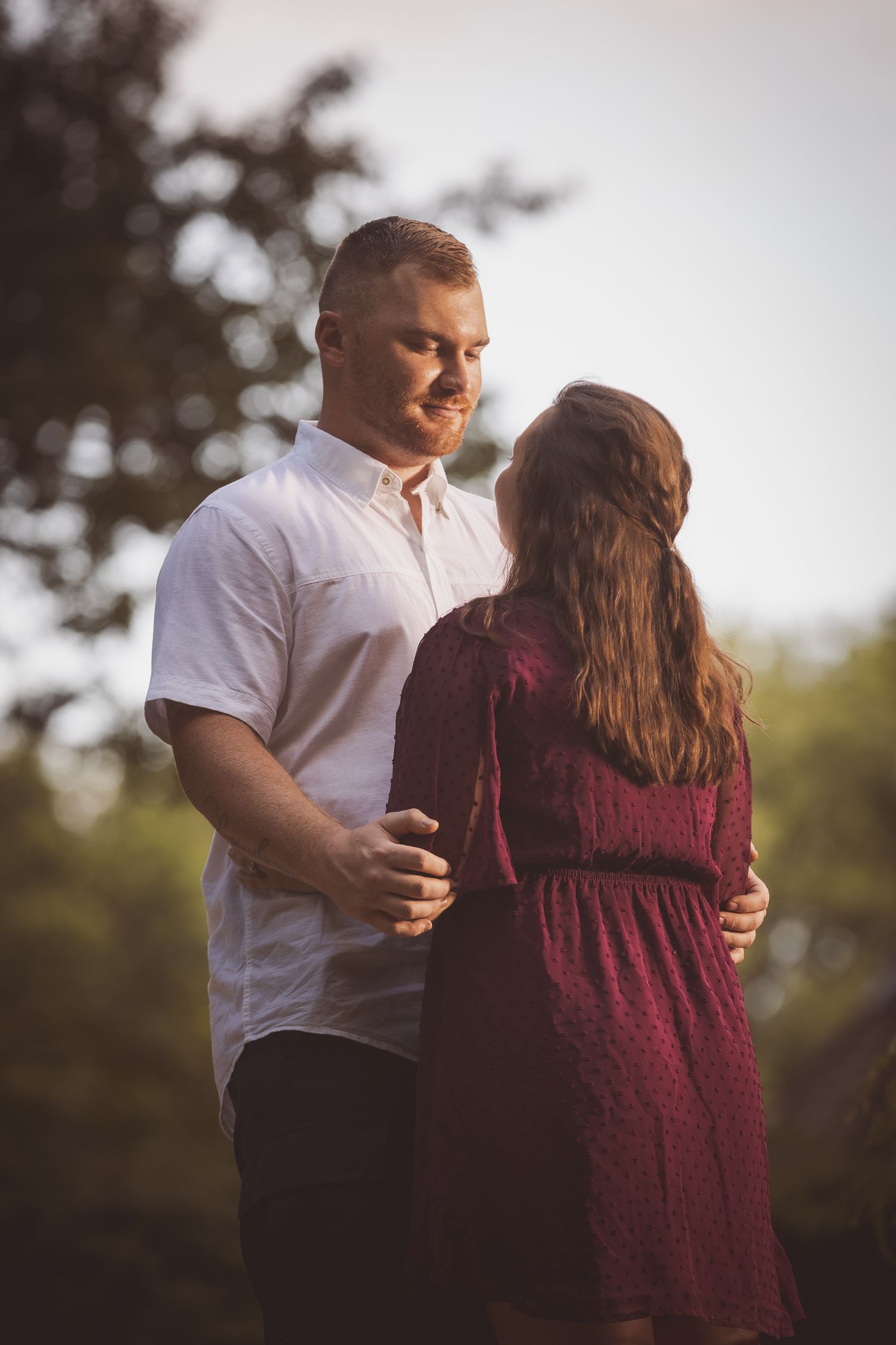 Couple embracing in warm sunset light, wearing burgundy and white.