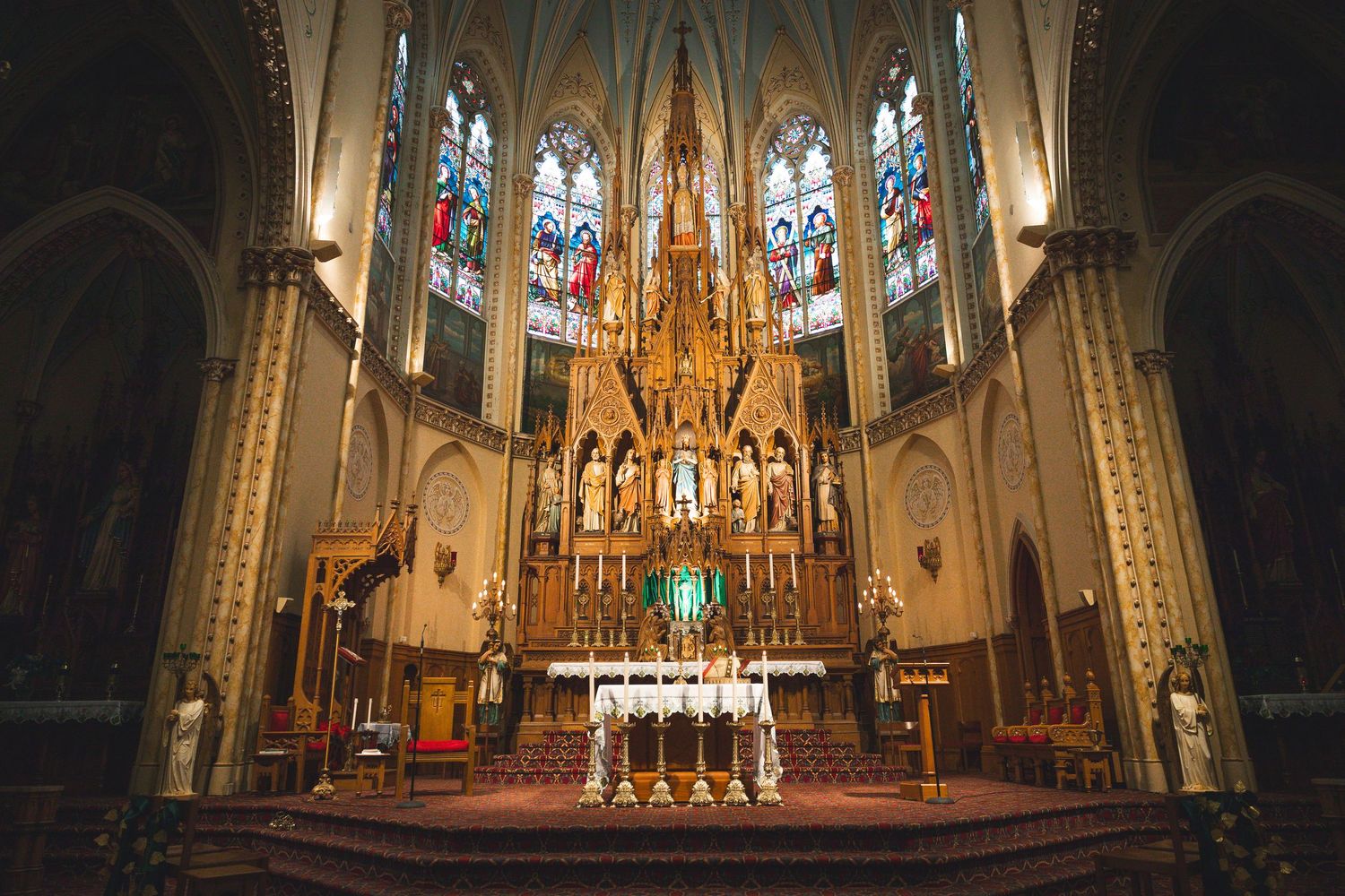 Interior of an empty gothic cathedral with stained glass windows and ornate golden altar.