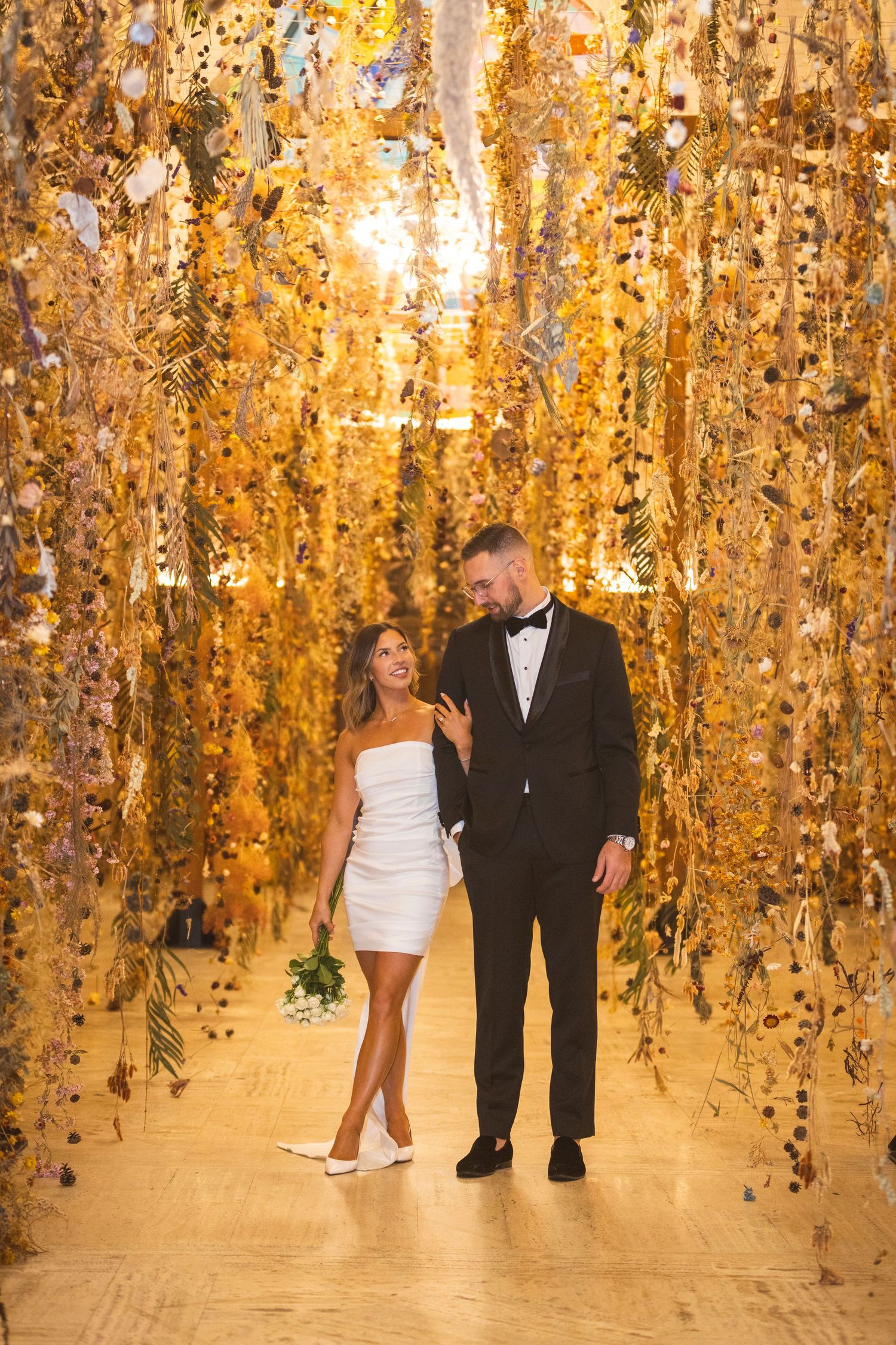 A romantic pose beneath golden hanging decorations in an elegantly lit indoor setting.