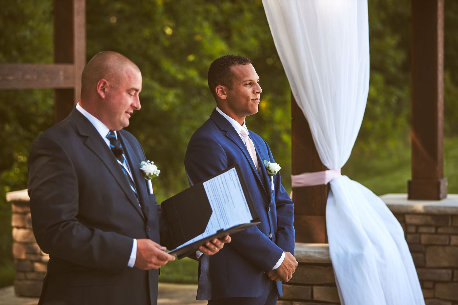 Wedding ceremony participants stand at an outdoor altar with white draping.