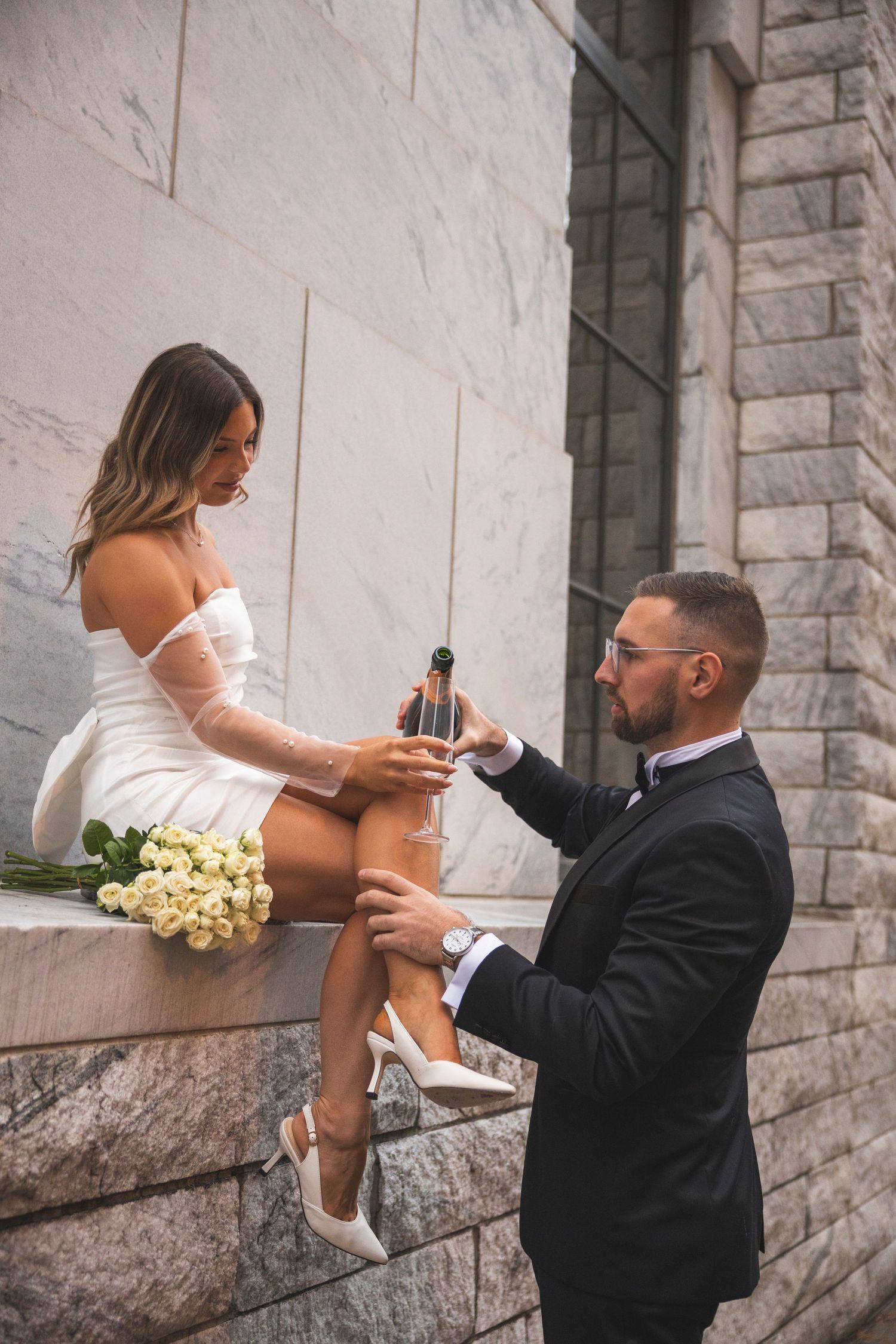 White bouquet and champagne celebration against stone wall backdrop.