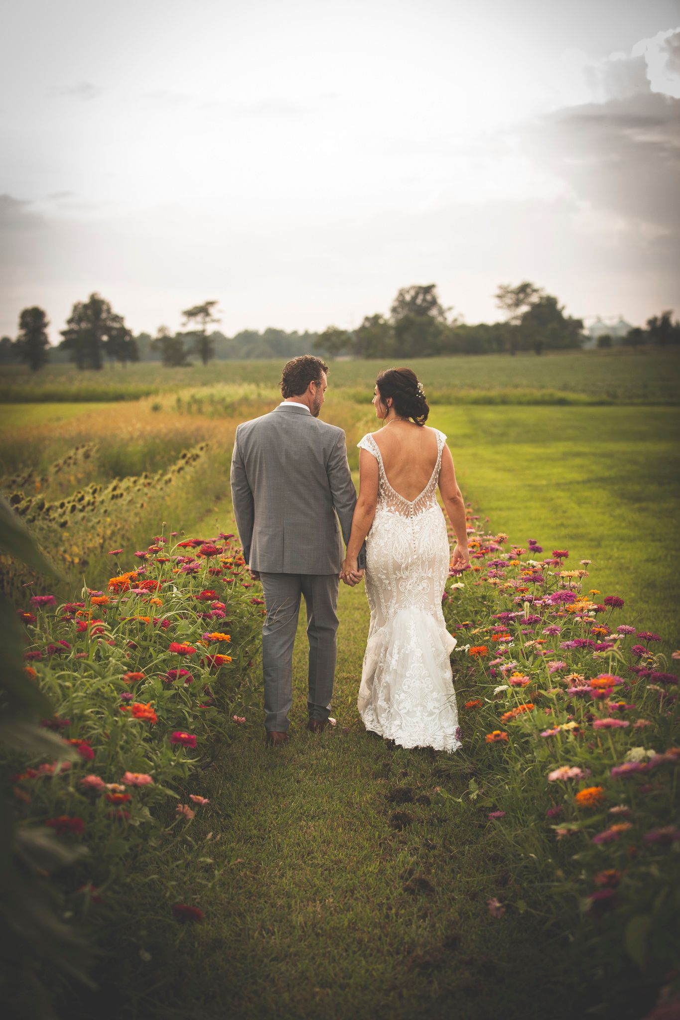 A couple walks through a field of red flowers on their wedding day.