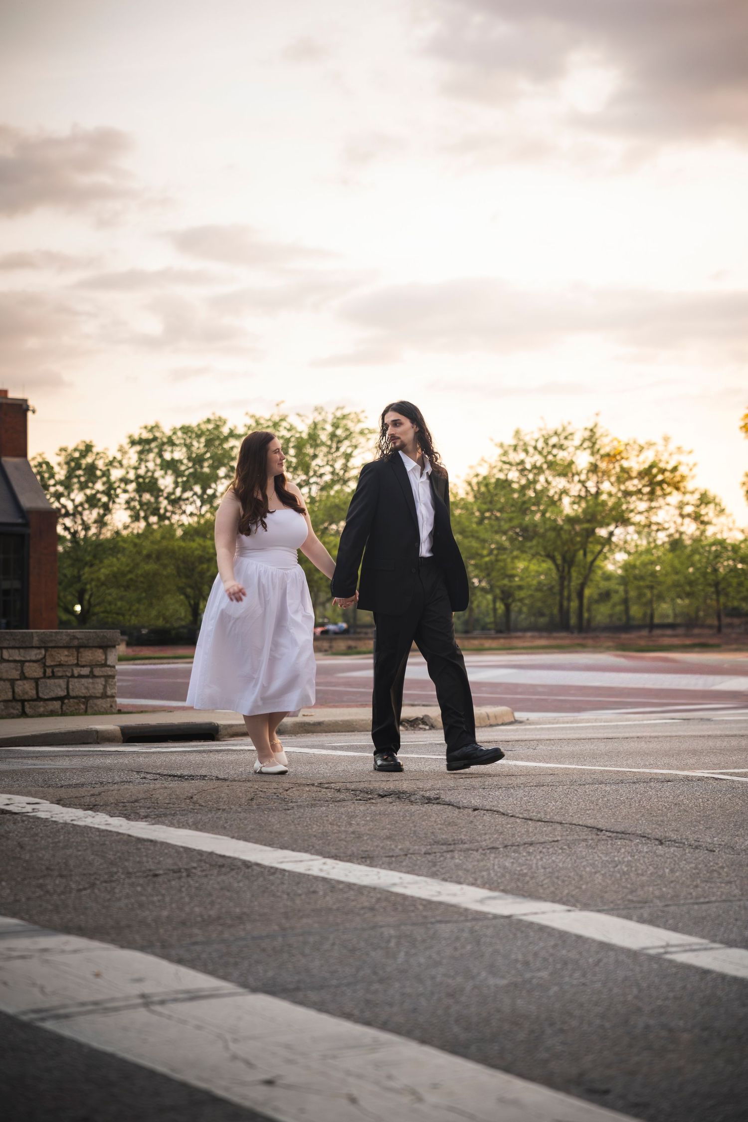 A couple in formal attire shares a tender moment at sunset in a parking area.