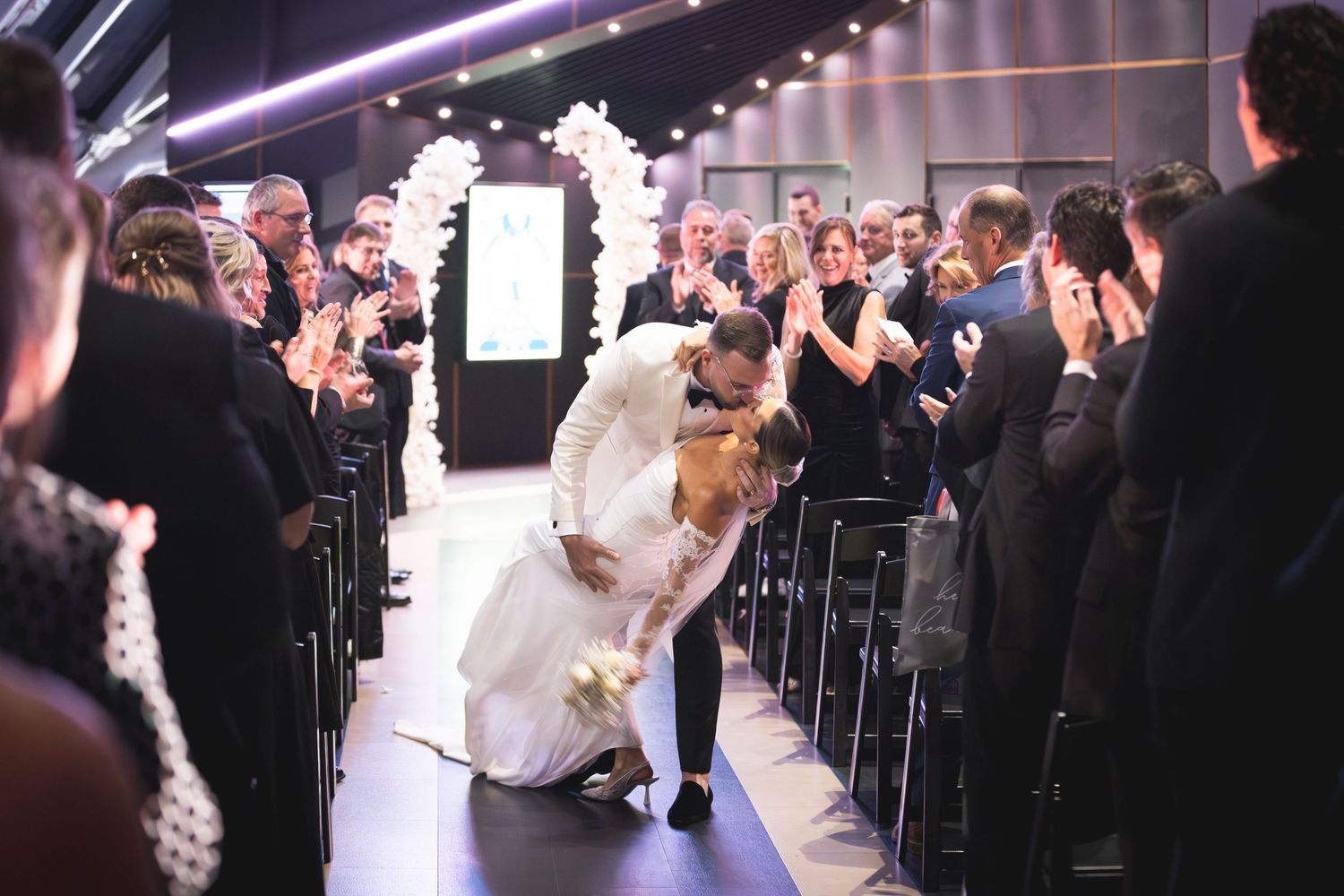 Wedding ceremony in progress with guests standing in formal attire.