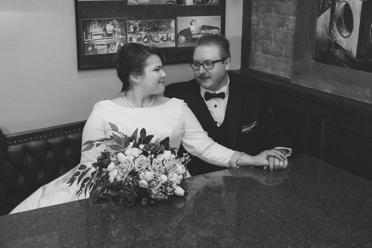 A black and white photo of a couple sitting at a restaurant booth with floral arrangements.