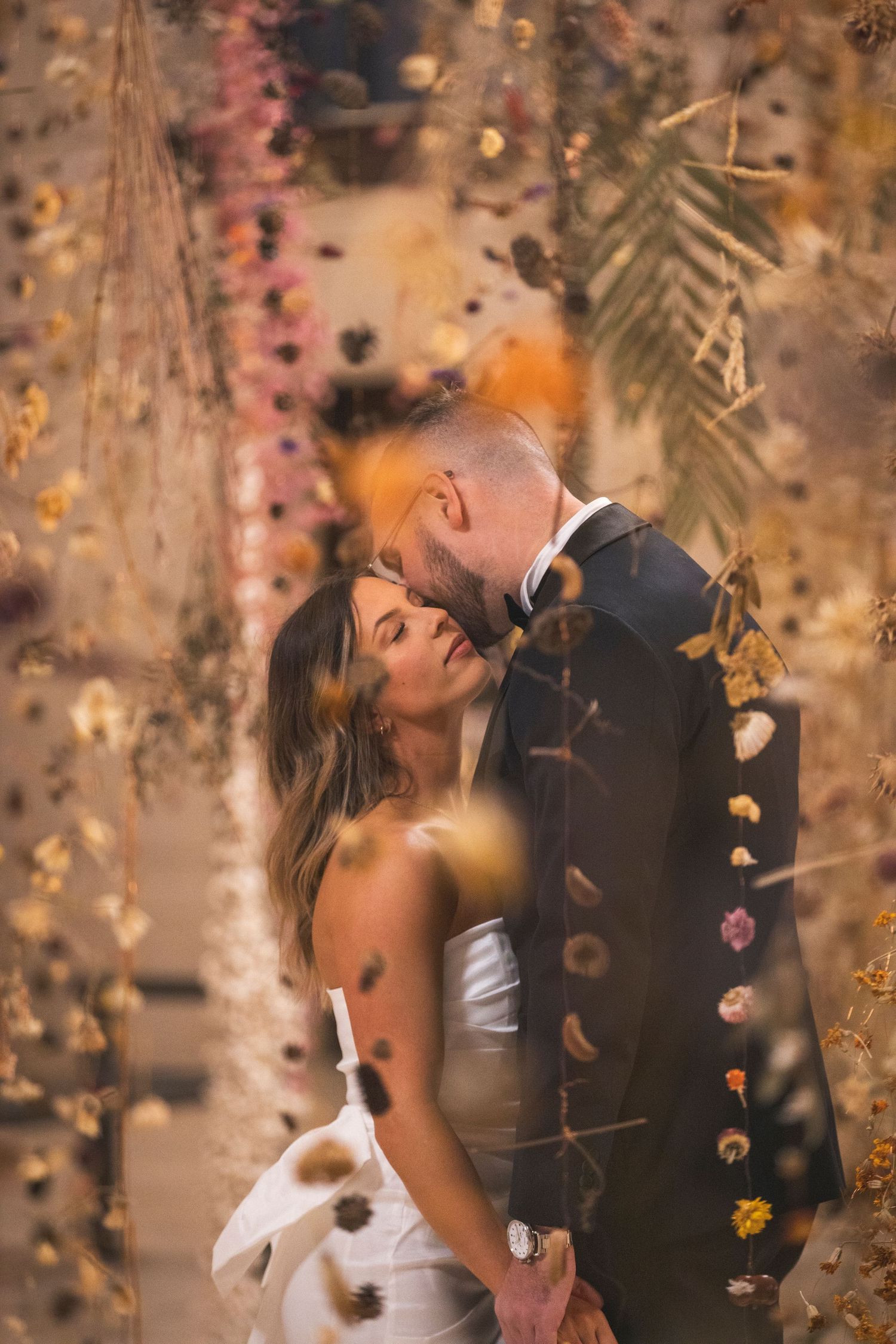 Romantic wedding moment under a canopy of autumn-colored leaves and flowers.