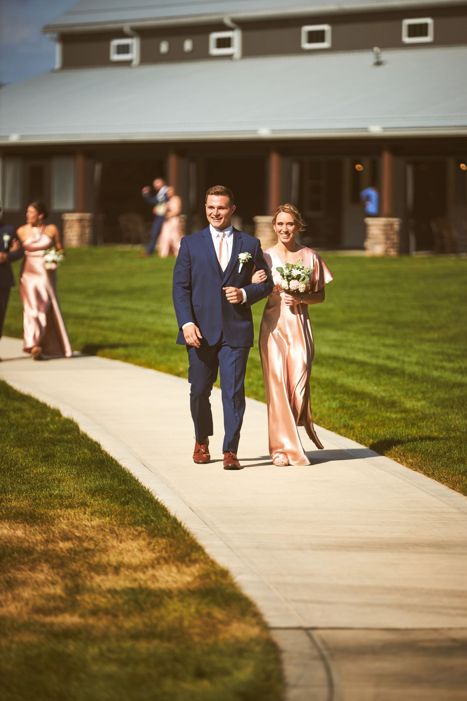 Wedding party members walk along a concrete path outside a building.