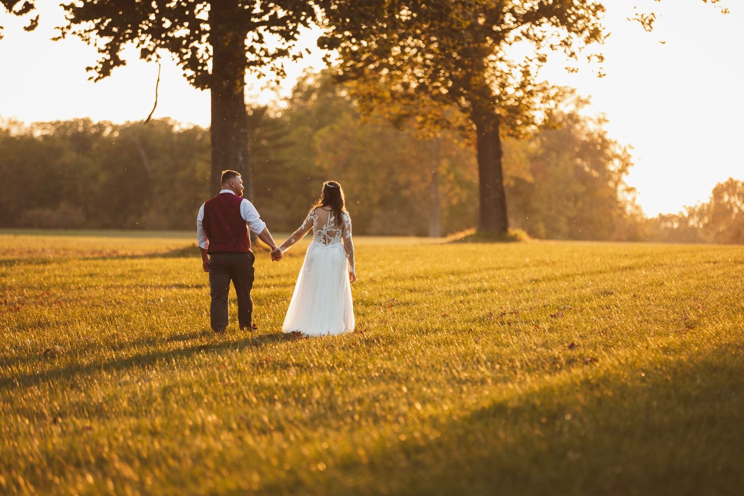 Golden sunset light streams through trees as couples walk across a grassy hilltop meadow.
