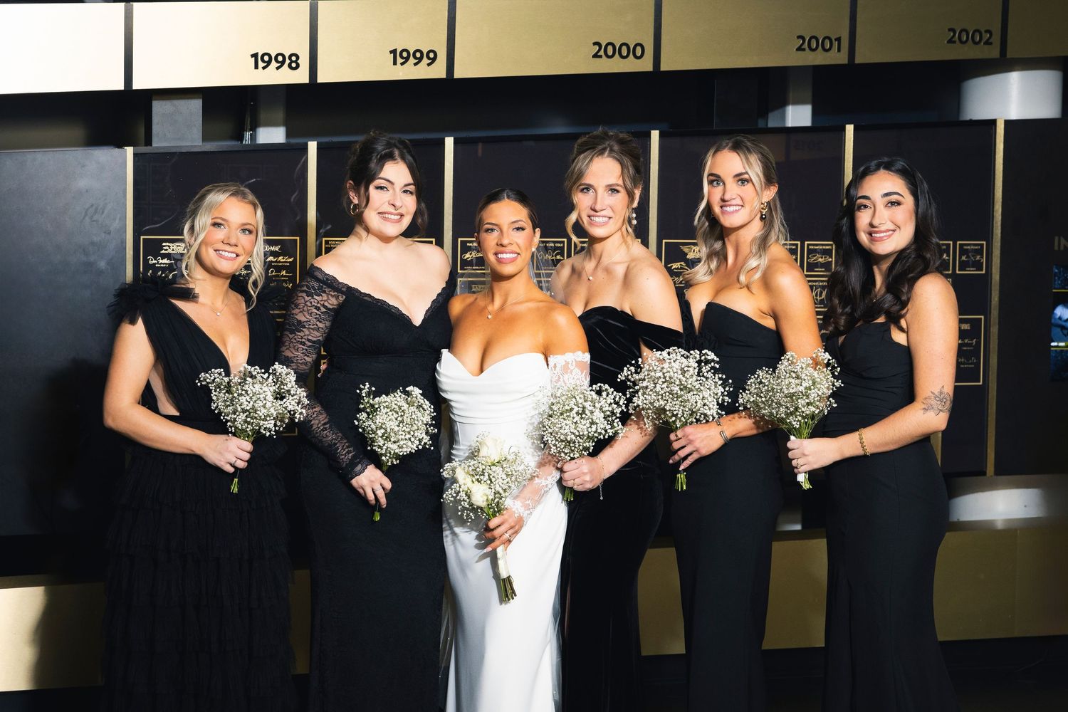 Wedding party poses together in formal attire against a timeline wall display.