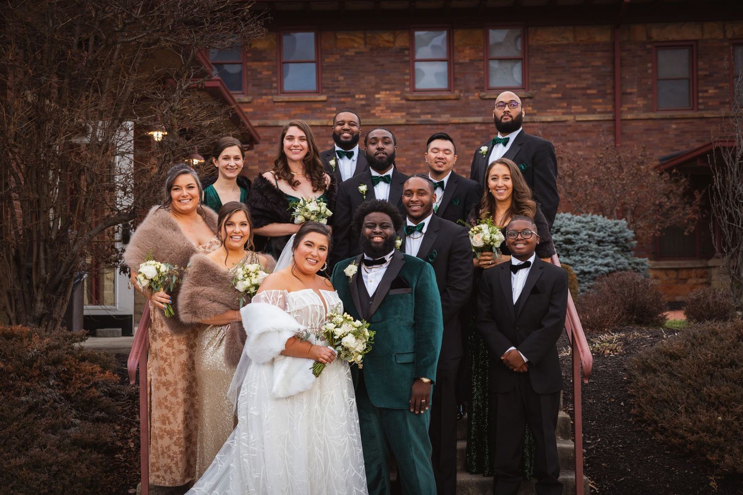 Wedding party poses elegantly against red brick architecture in formal attire.