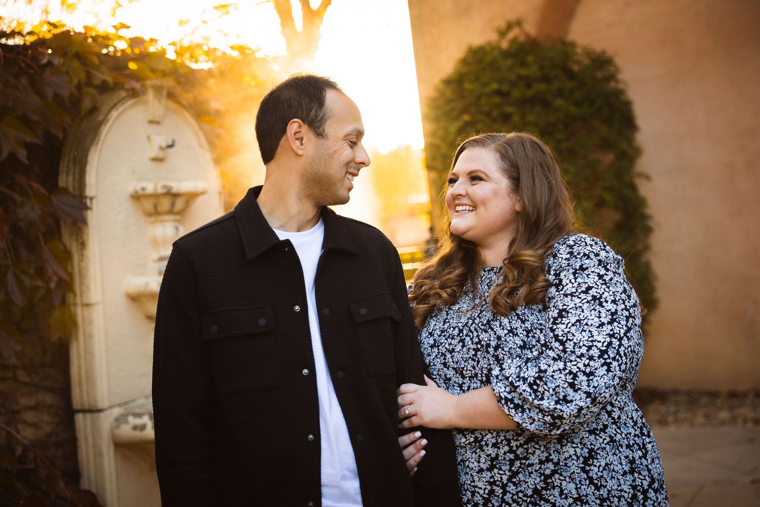 A couple shares a romantic moment in an elegant stone archway during golden hour.