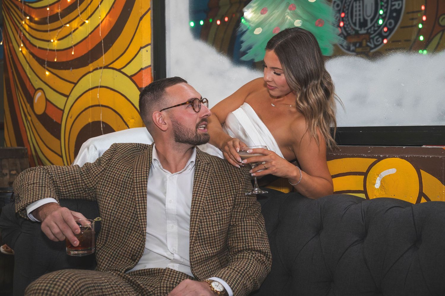Newlyweds sharing an intimate moment in a cozy restaurant with festive lighting and decor visible in the background.