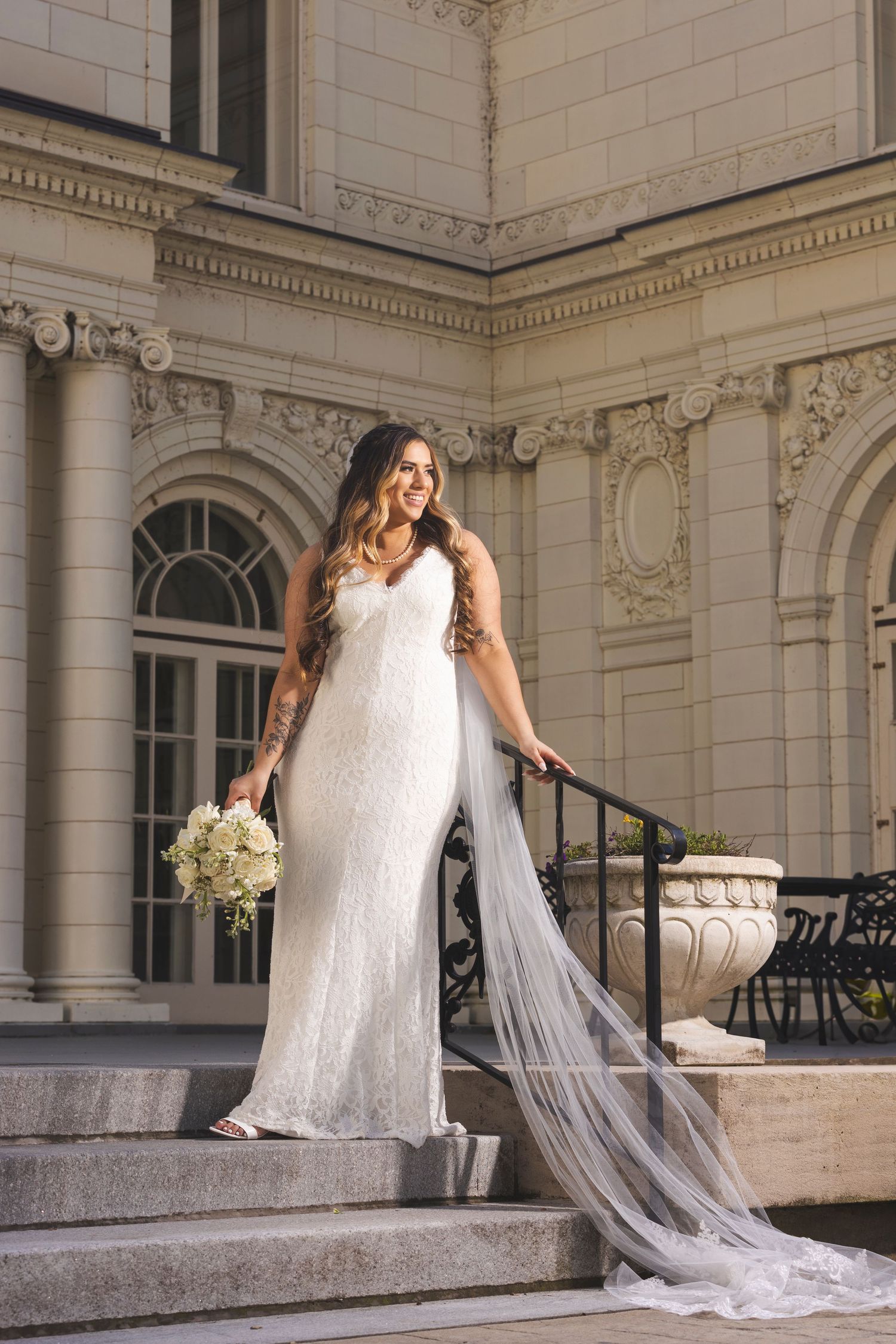 Elegant wedding dress with long flowing veil photographed on classic architectural steps.