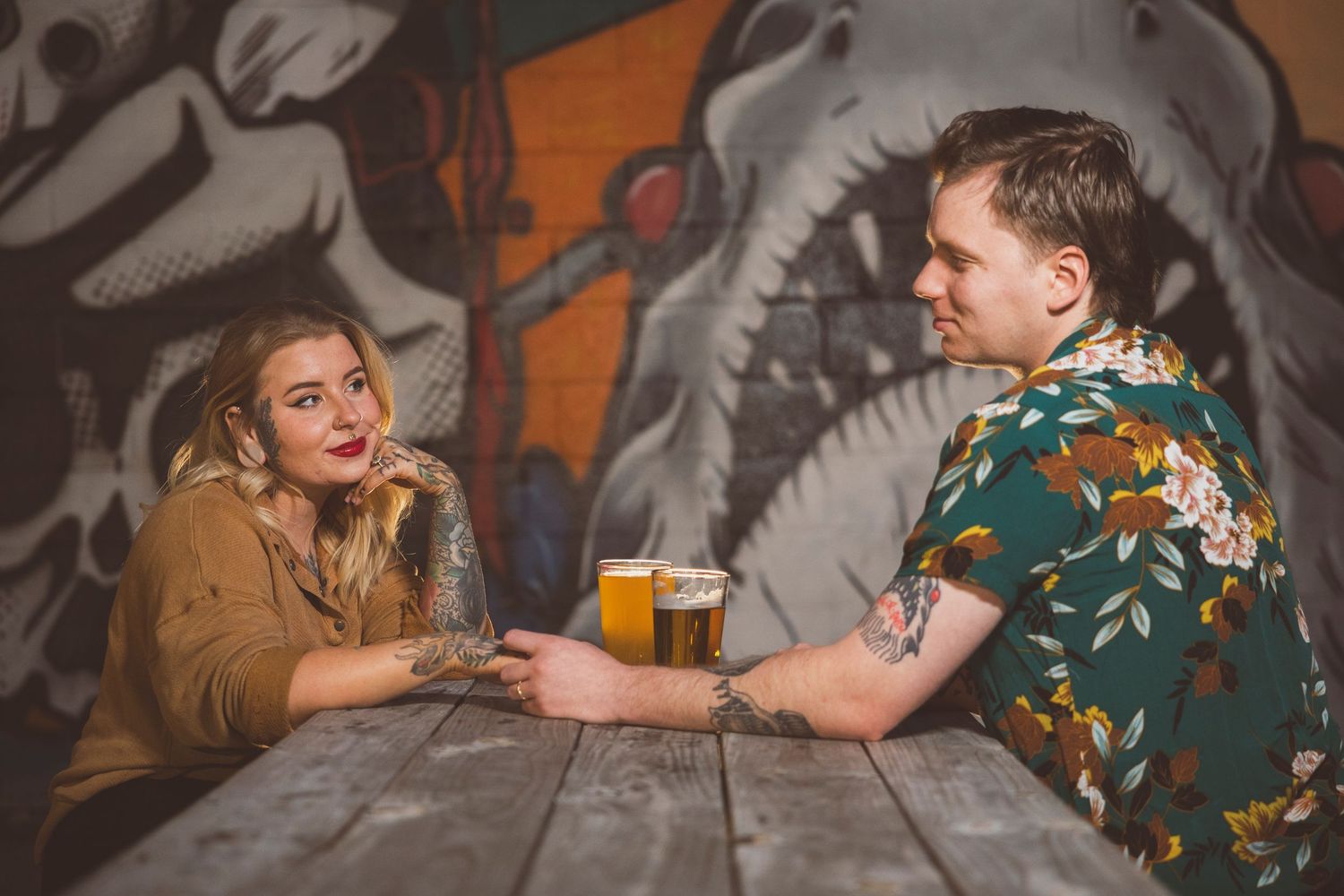 Couple sitting at bar with colorful drinks and anime posters on wall.