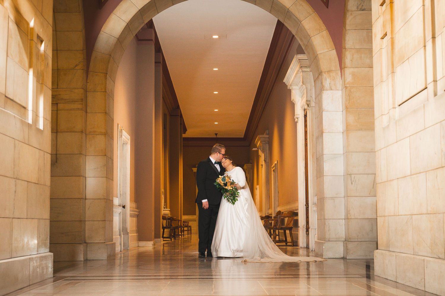 Sunlit stone corridor with arched ceilings and classical architectural details.