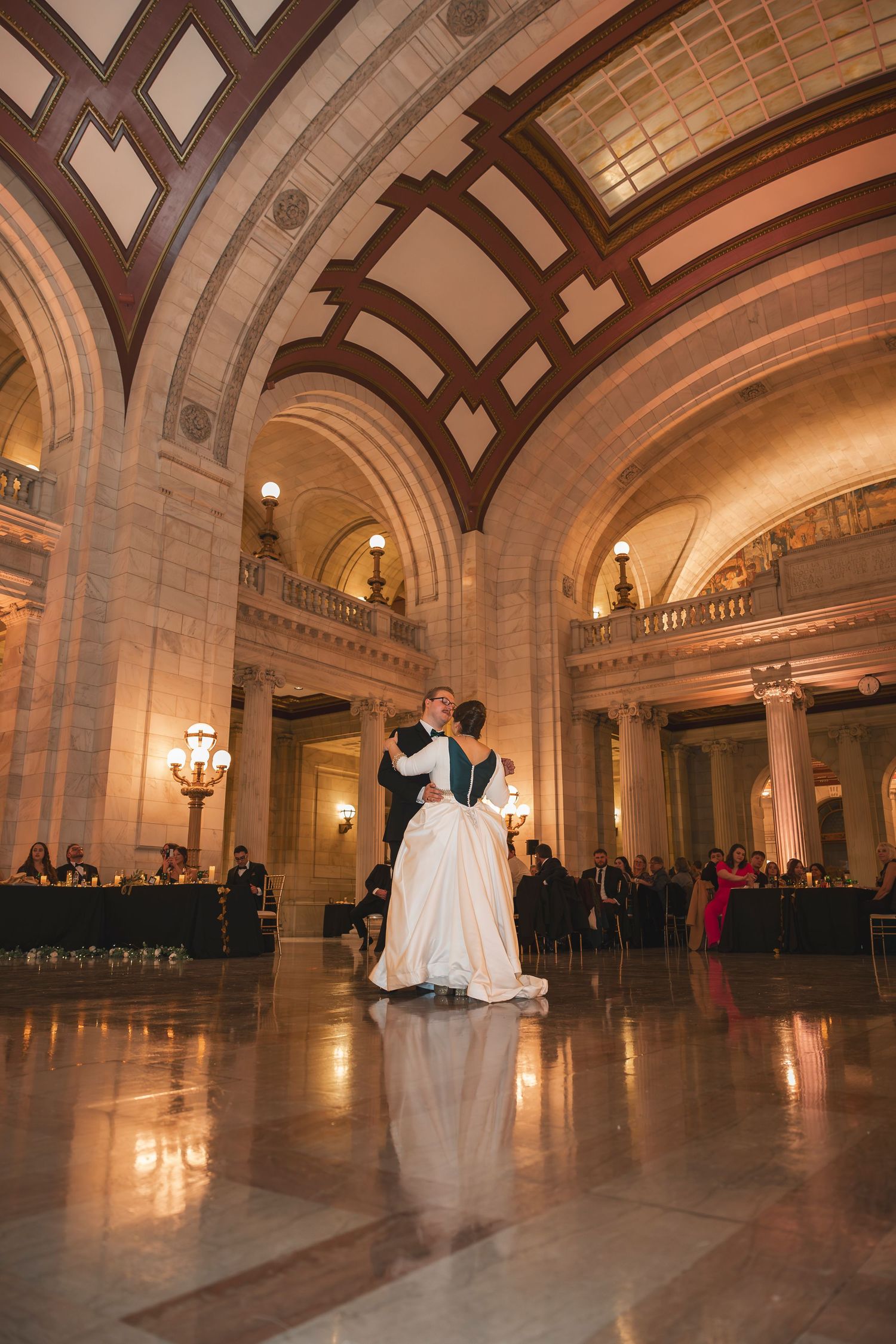 Spacious ballroom with arched ceilings and polished floors reflecting ambient lighting during a wedding.