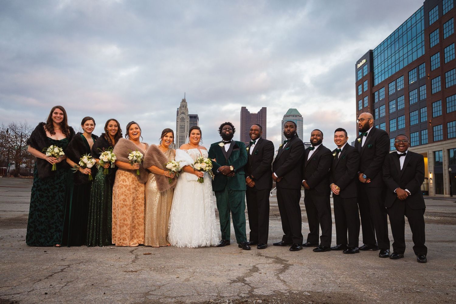 Wedding party group photo with cityscape backdrop and modern buildings.