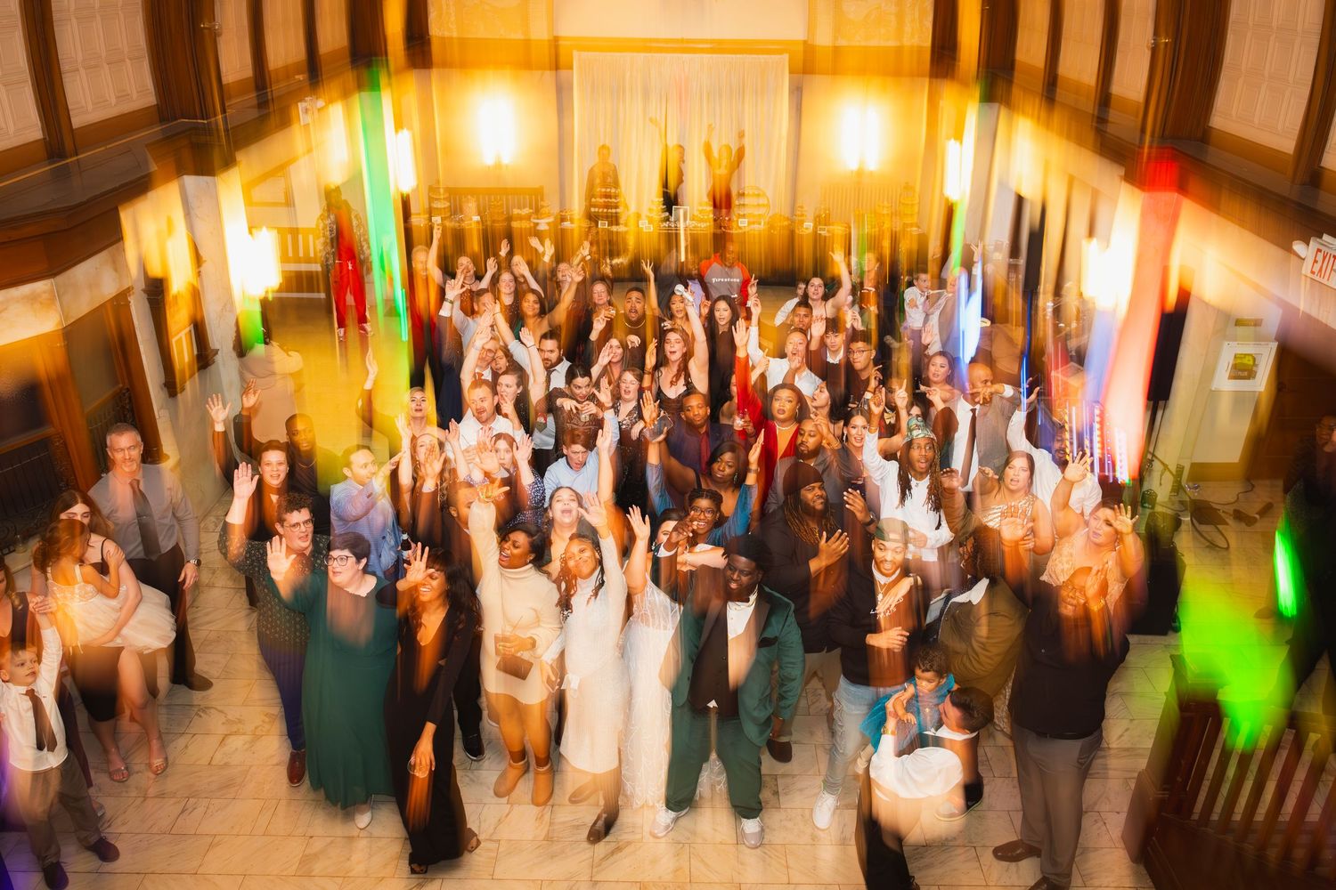Wedding guests fill a grand ballroom dance floor during an evening celebration.