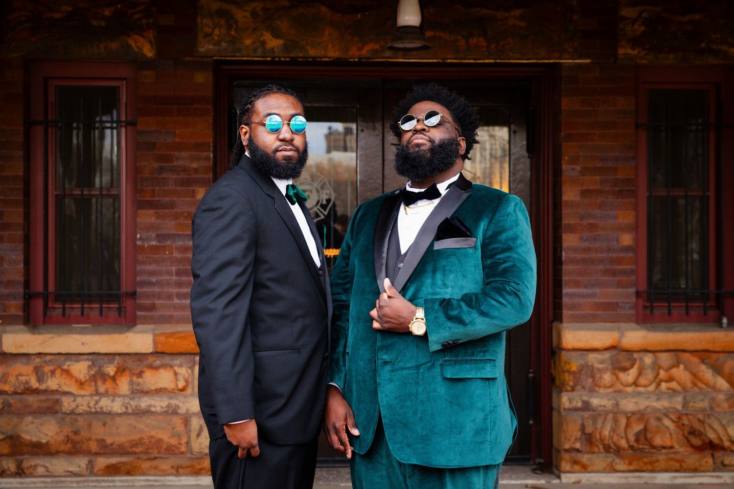 Groomsmen in emerald and black suits interact playfully outside venue.