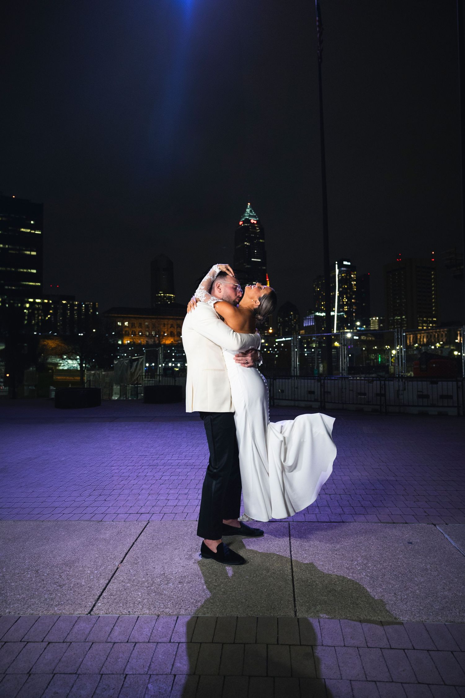 A dramatic dip dance move performed on purple-lit pavement at night.