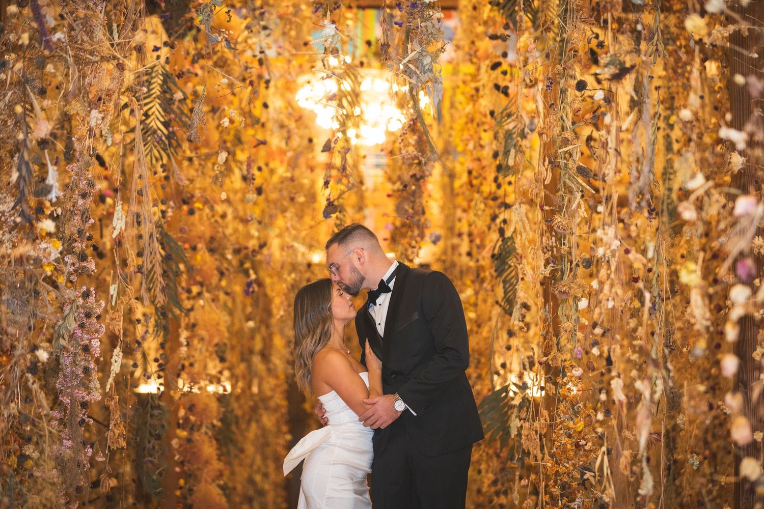 Wedding couple embraces in front of golden autumn foliage at sunset.