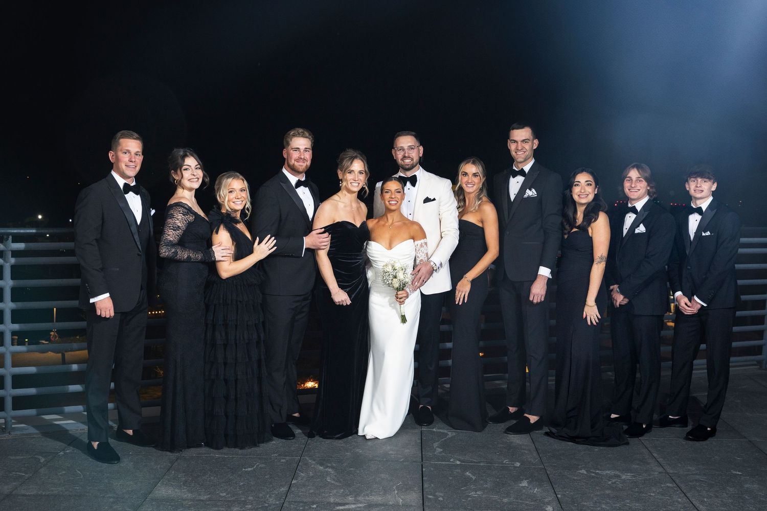 Large wedding party poses together in formal attire at modern venue space.