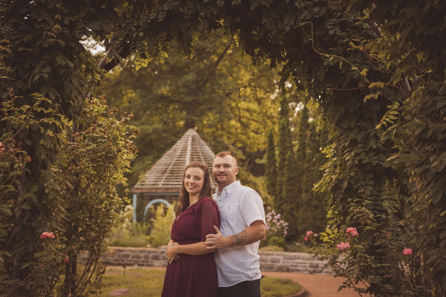 A couple shares an intimate moment under trees in a tranquil garden setting.