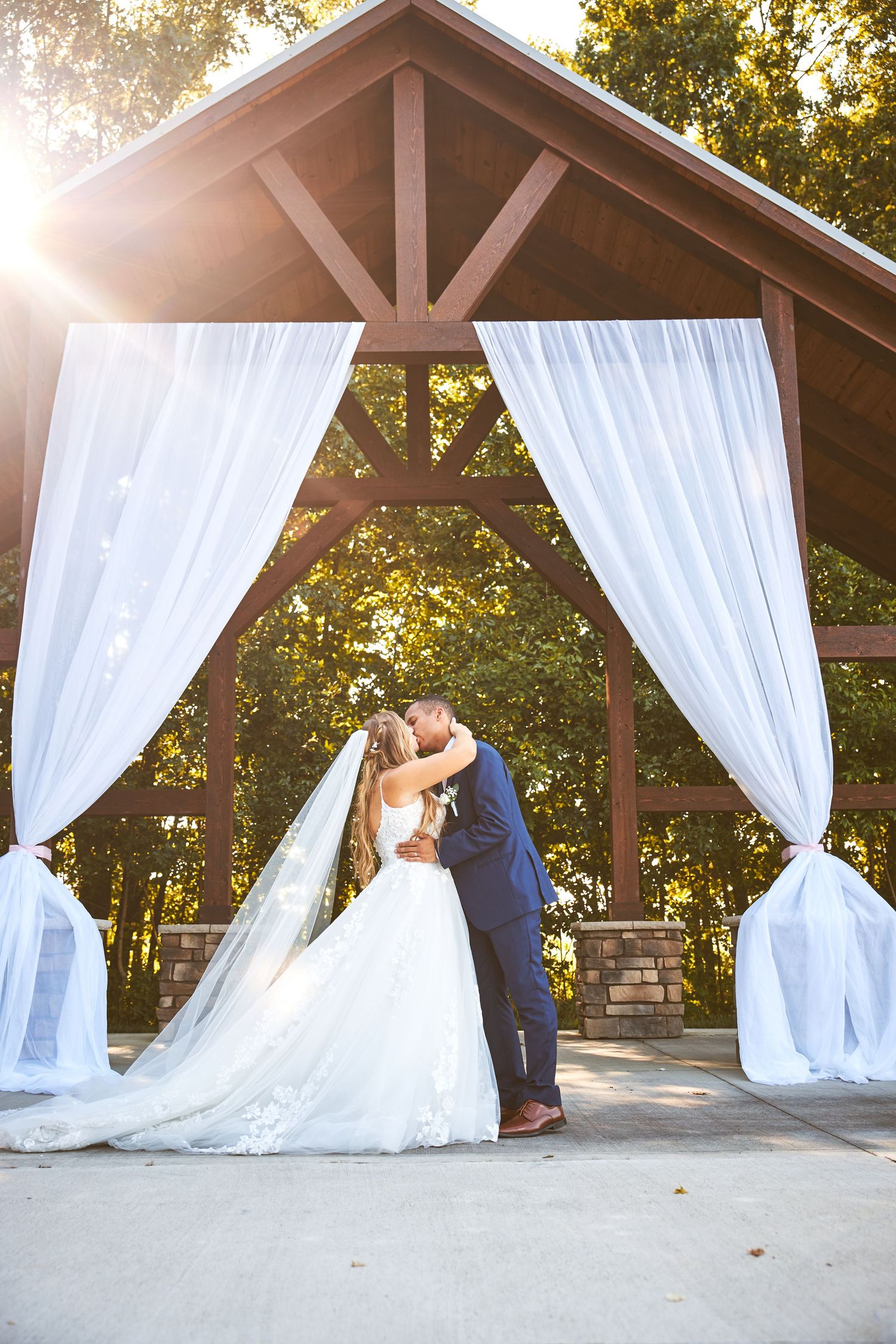 Wedding couple sharing romantic moments under flowing white drapes at an outdoor venue.