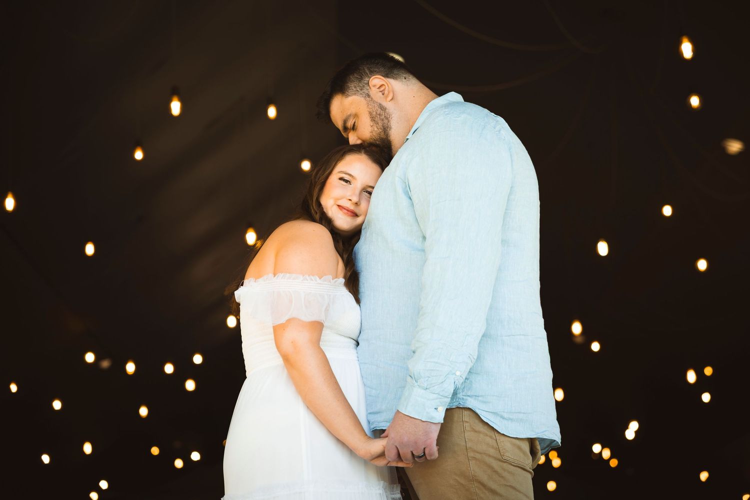 A couple dances under twinkling string lights in a dimly lit venue.
