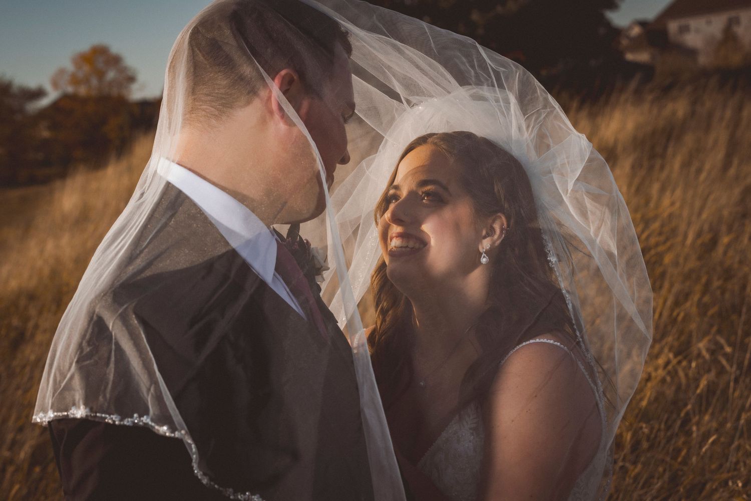 Wedding portraits at golden hour with flowing veil in tall grass field.