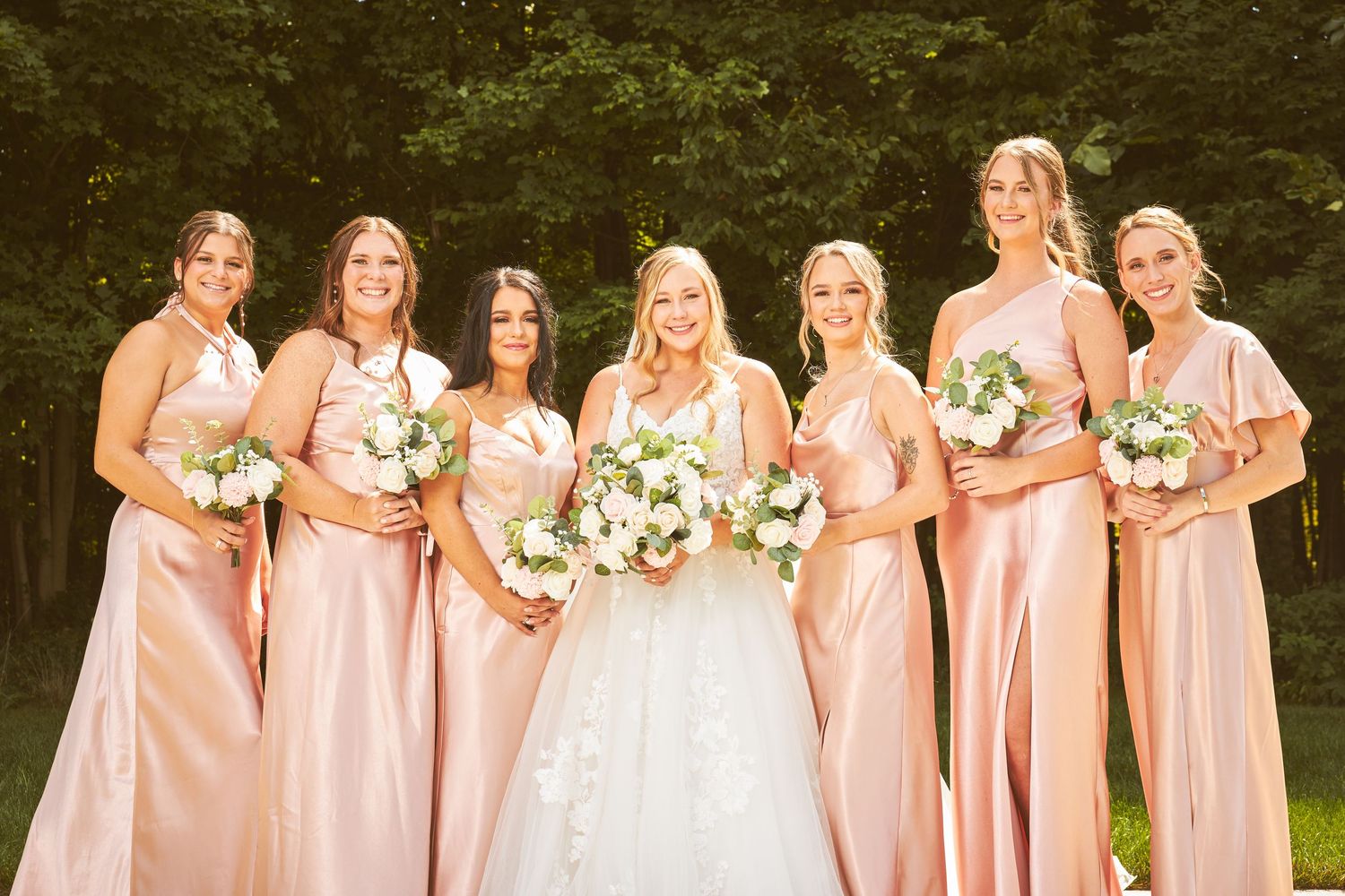Bridal party in pink dresses pose together on a sunny outdoor terrace.