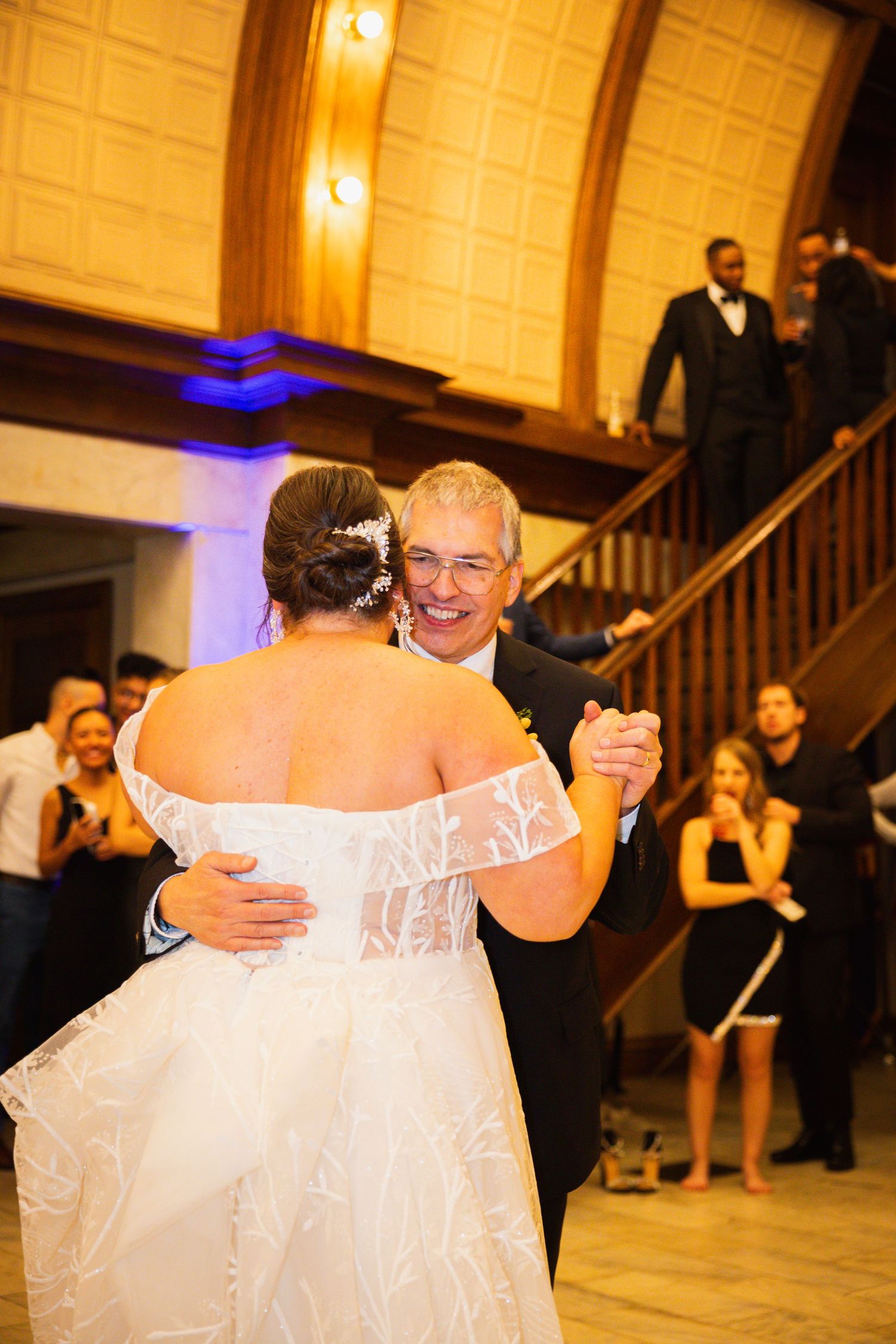 A heartfelt father-daughter dance moment captured during a wedding reception in a warmly lit ballroom.