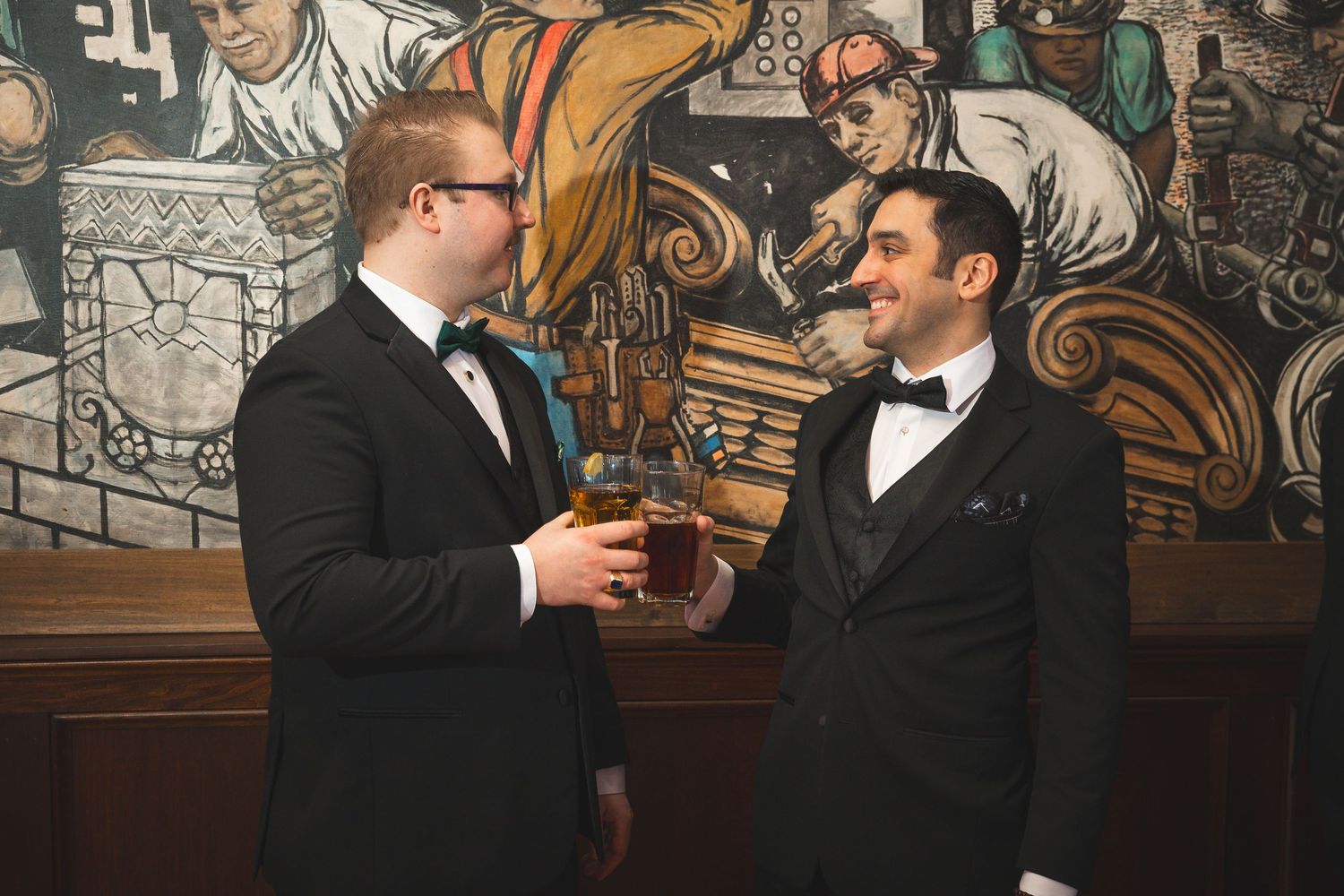 Two people in formal attire sharing a candid moment against an artistic wall mural.
