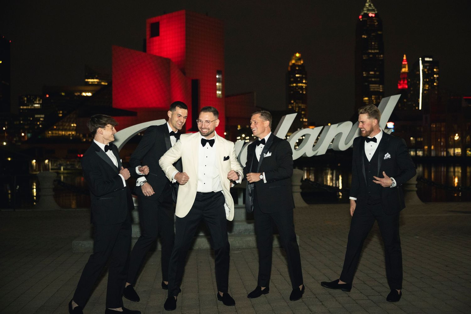 Wedding party poses for dramatic nighttime photos against city lights.