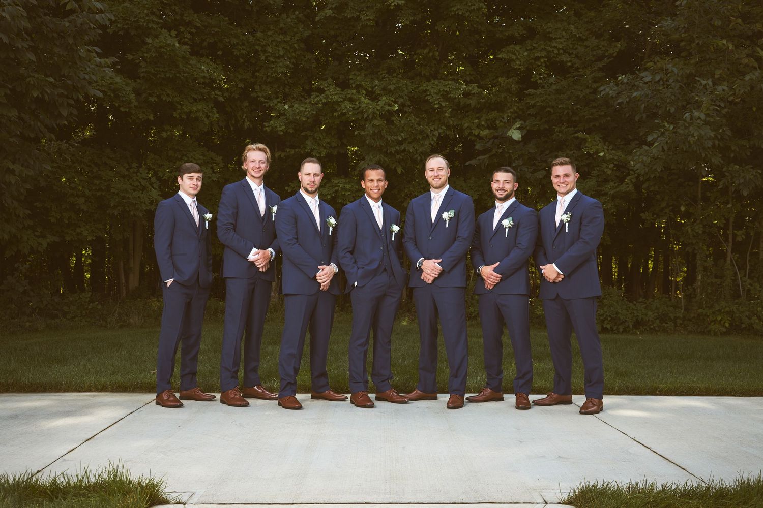 Wedding party members in matching navy suits lined up for formal outdoor portrait.