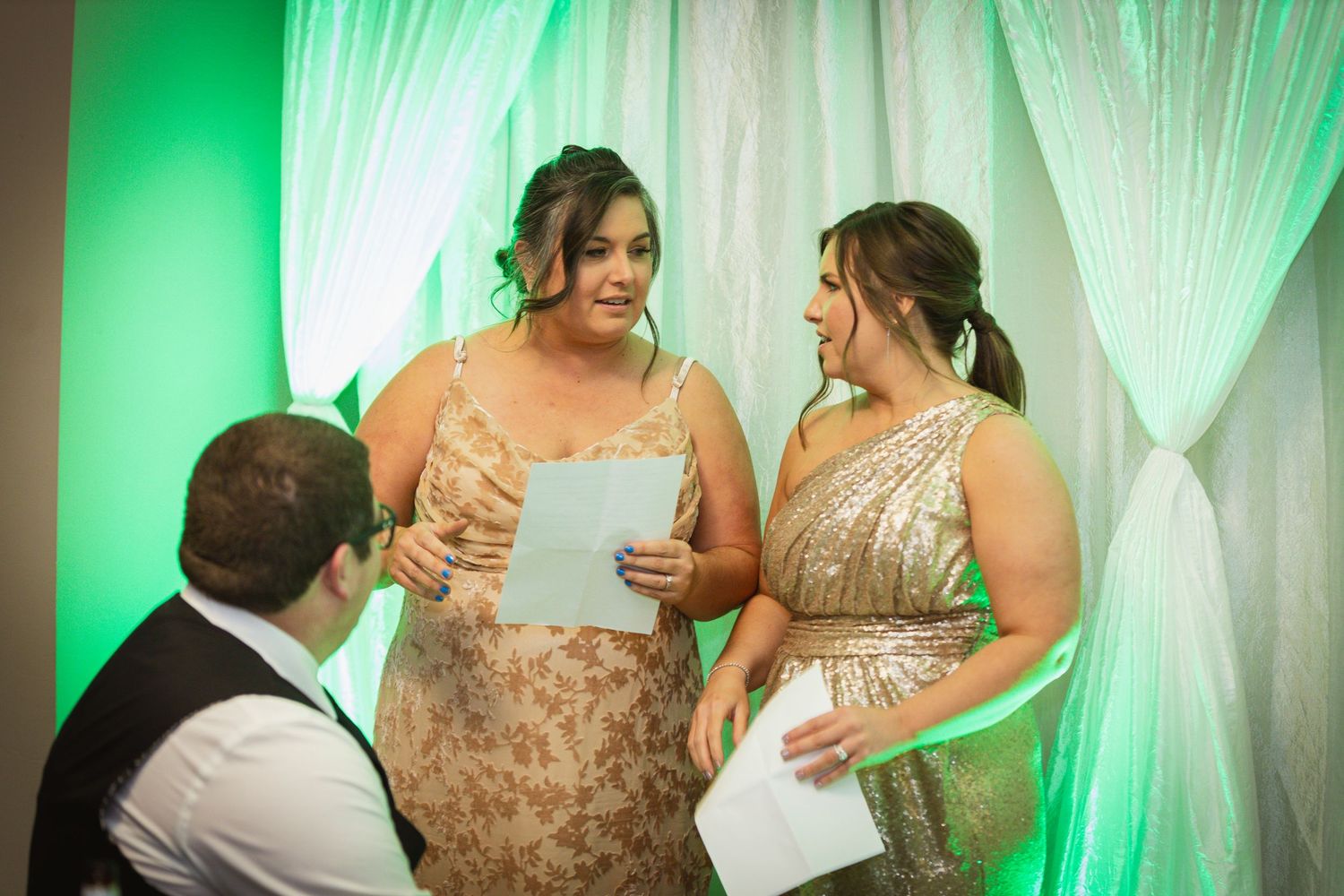 Wedding reception area with elegant white draping illuminated by green accent lights.