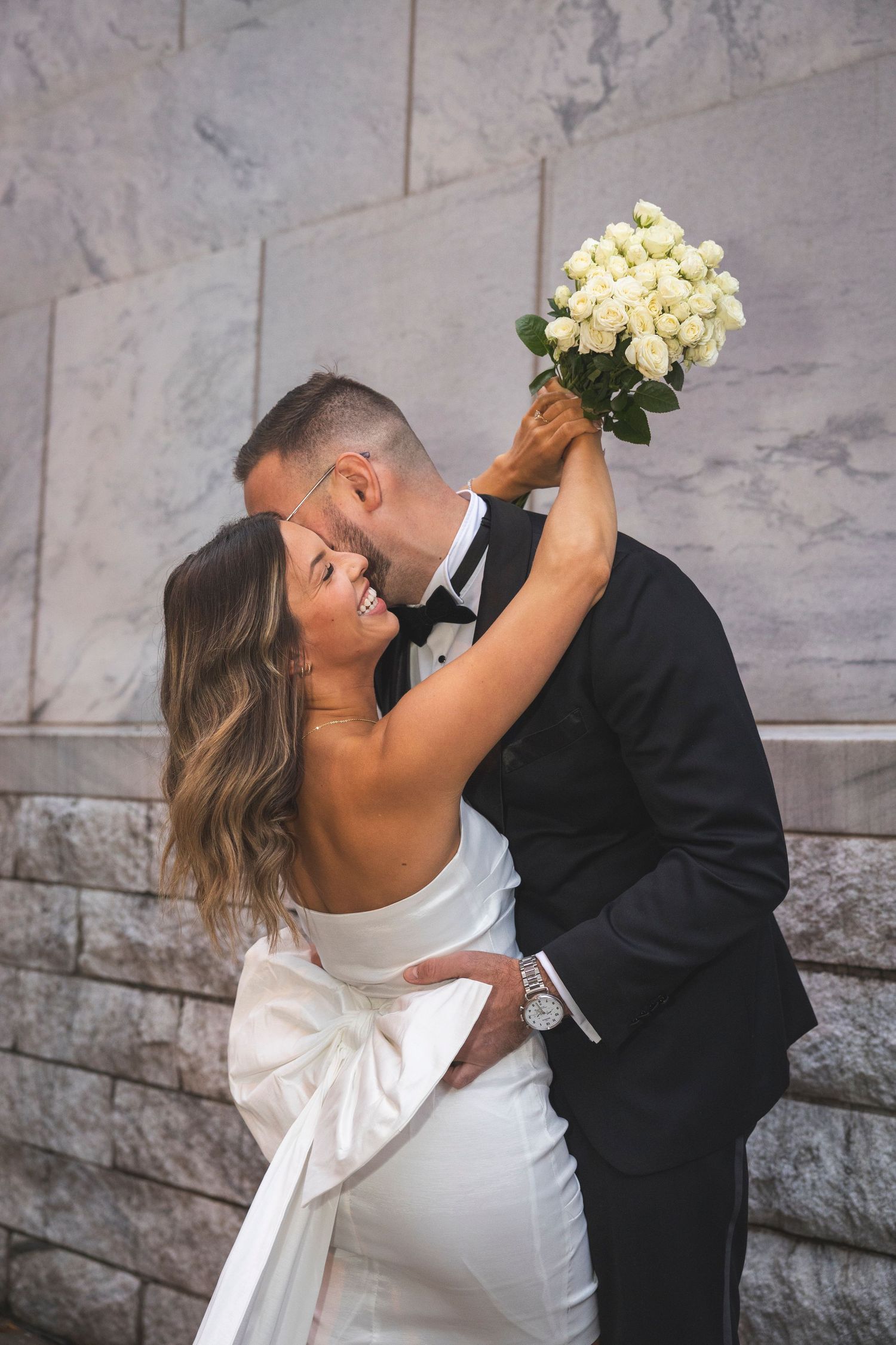 A joyful wedding moment with the bride holding up her bouquet while sharing an intimate moment.