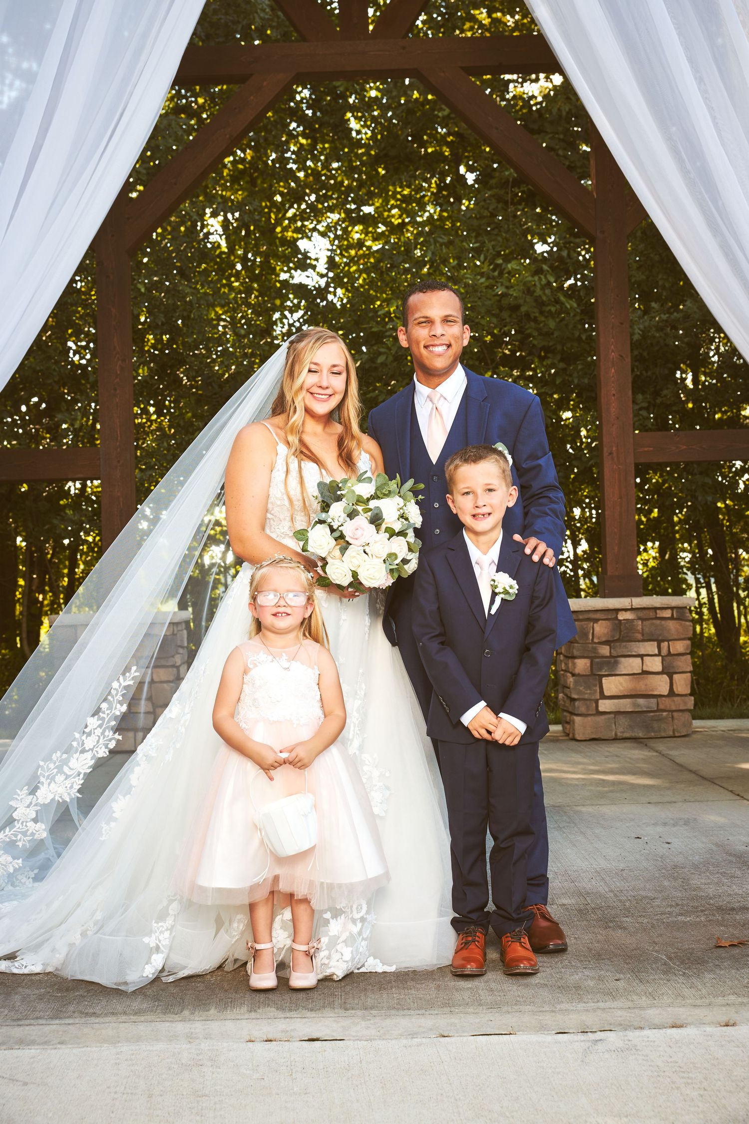 Wedding party poses under white drapes at an outdoor ceremony venue.