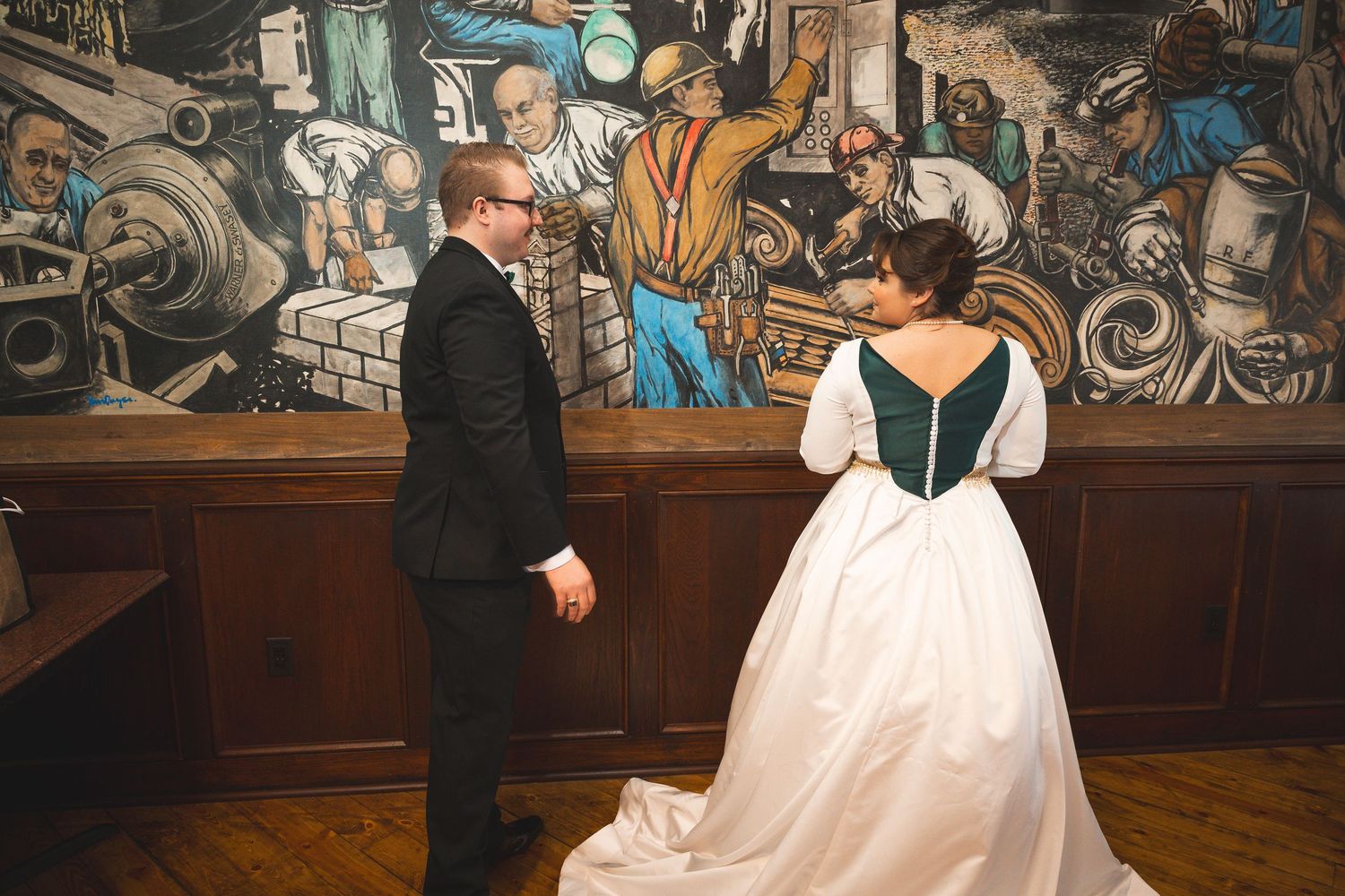 A couple stands in front of a colorful mural during their wedding celebration.