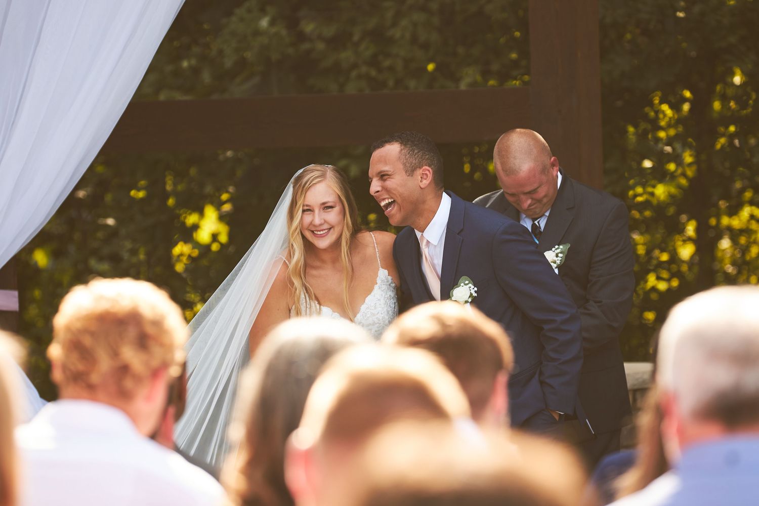 A wedding celebration under a wooden pergola with flowing white curtains.